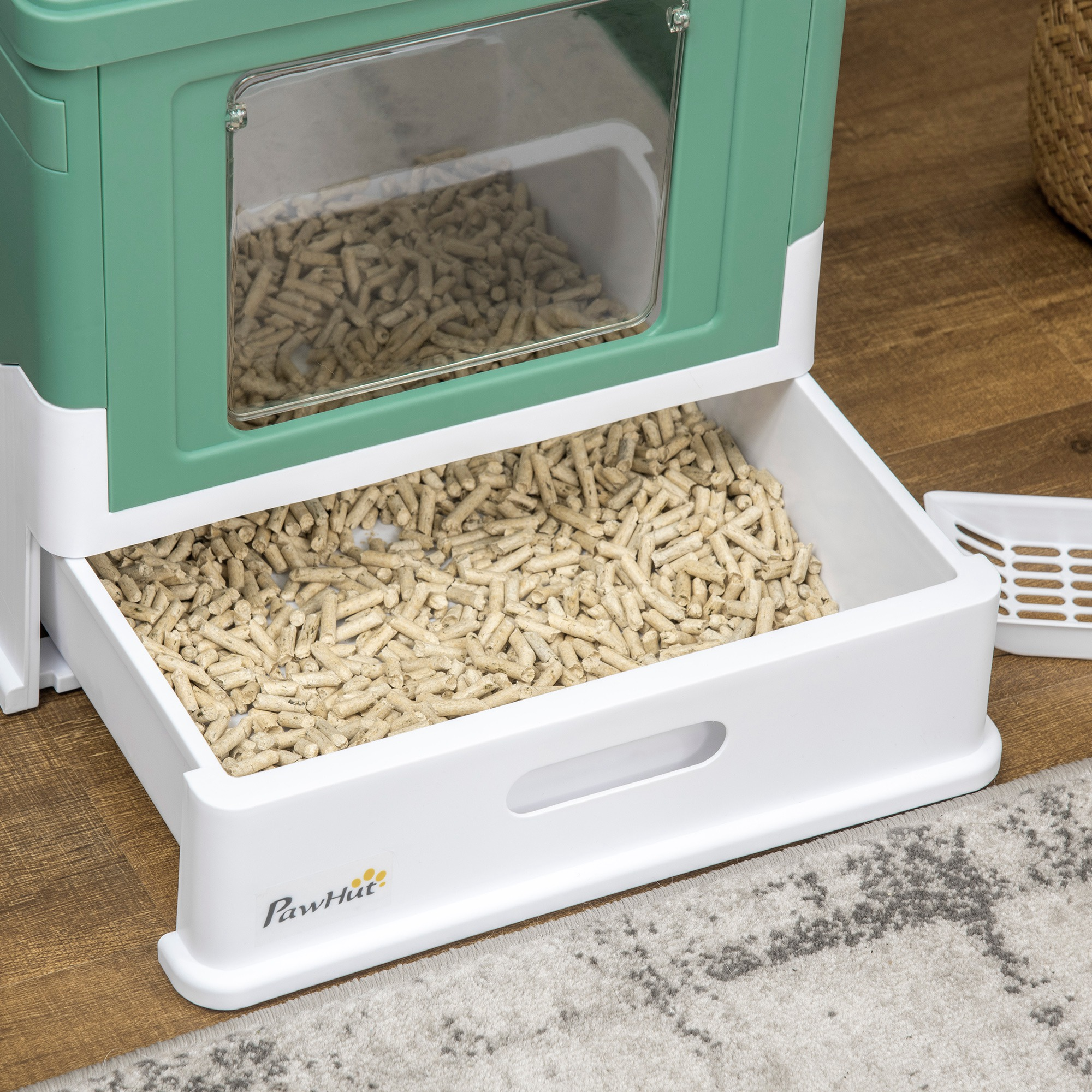 Una caja de arena blanca y verde con pellets de madera en el interior y un cajón extraíble.