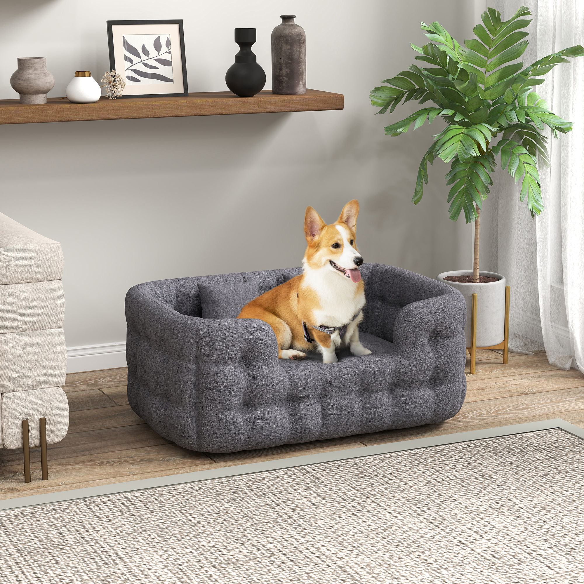 Un perro en una cama gris para perros en una habitación con una planta y una estantería con decoración.