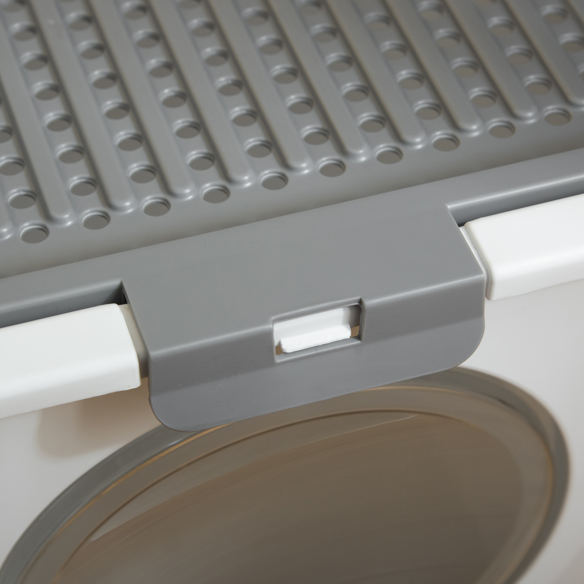 Primer plano de una caja de arena gris y blanca con una rejilla gris y un pestillo blanco.