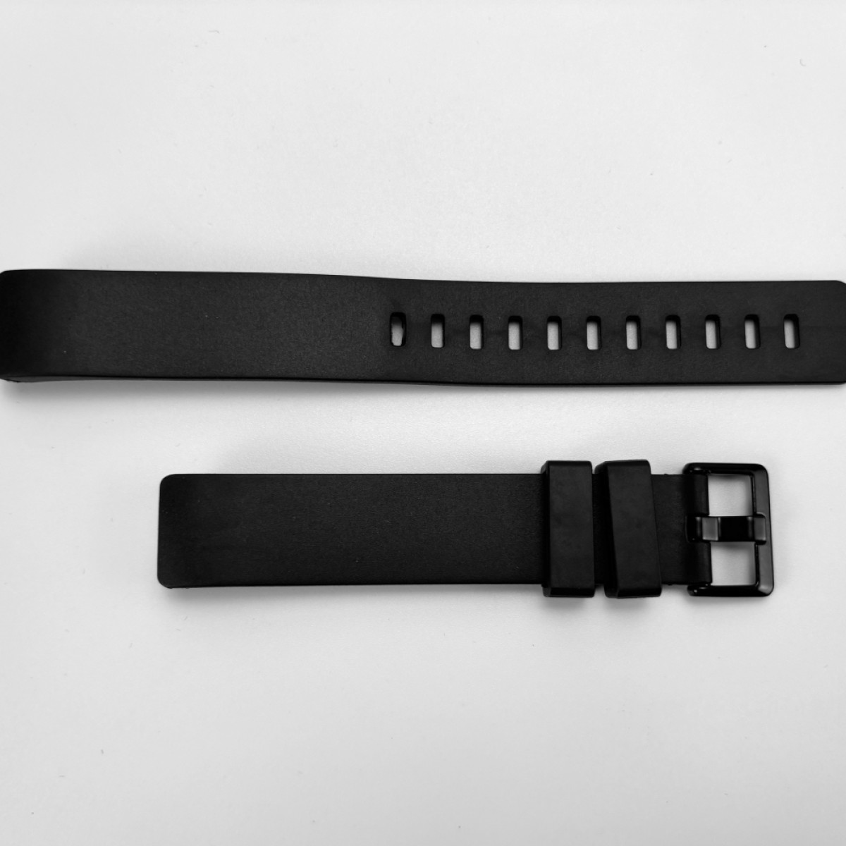 Zwei schwarze Armbänder liegen auf einer weißen Oberfläche. Eines hat Löcher, das andere eine Schnalle.
