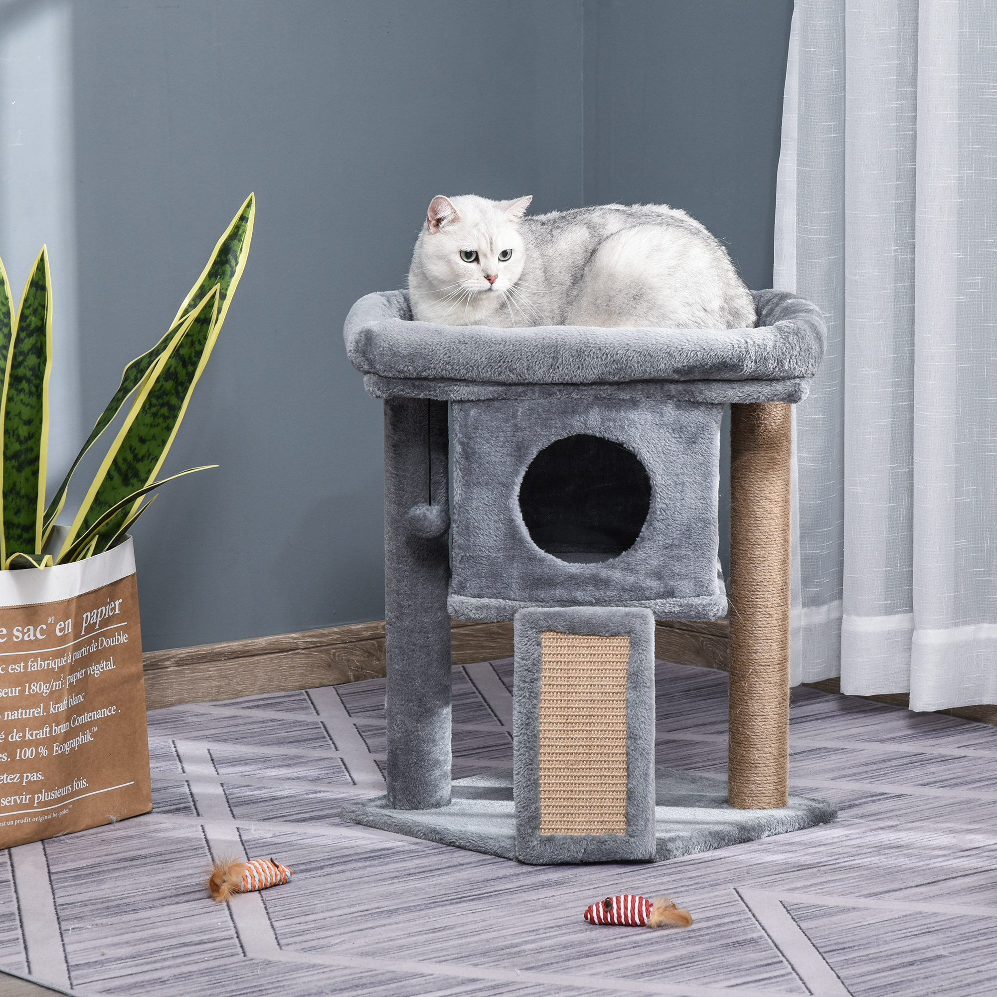 Un gato gris está sentado en un árbol para gatos gris con un agujero y un rascador en una habitación.