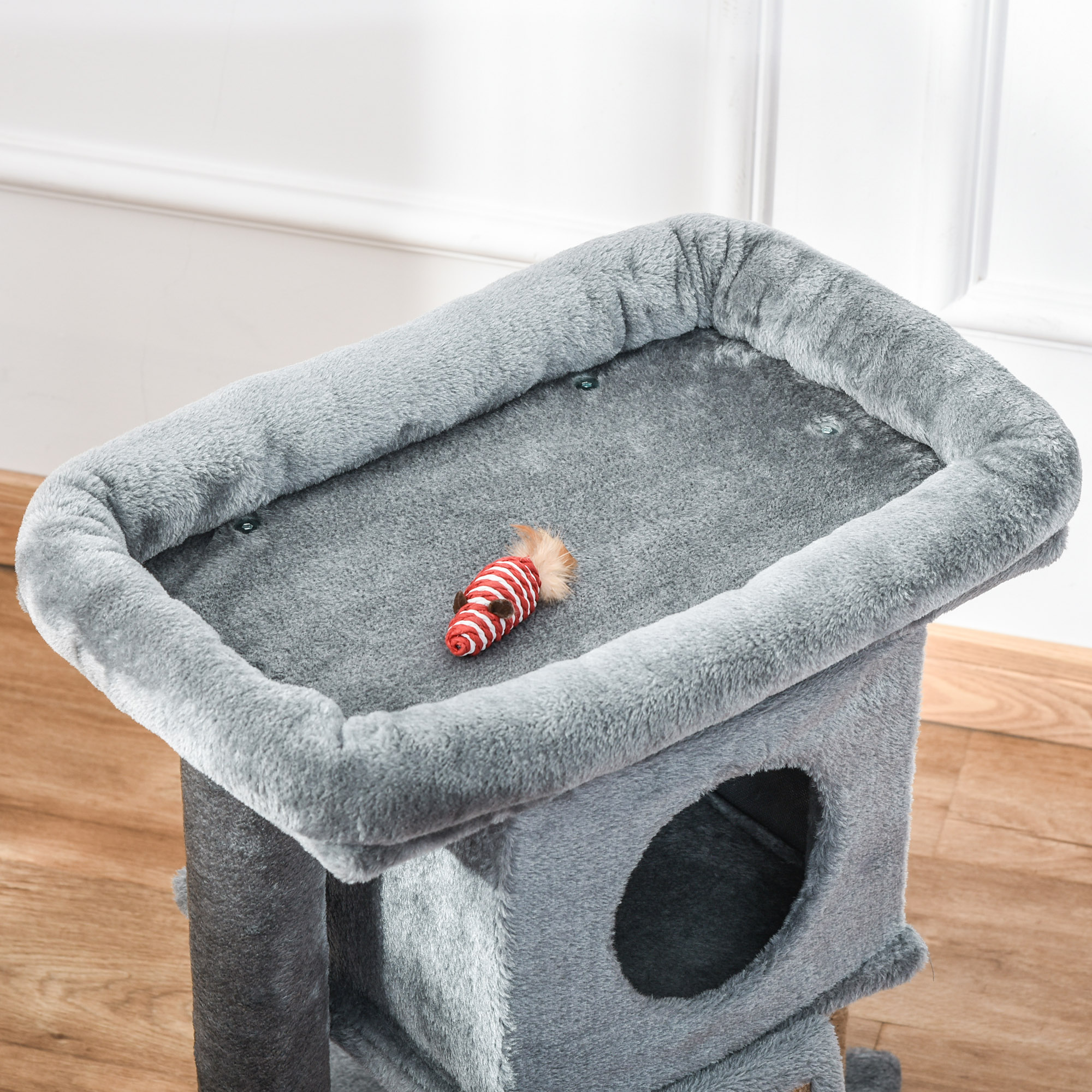 Un árbol para gatos con un ratón de juguete y una plataforma gris acolchada. También hay una madriguera para gatos.