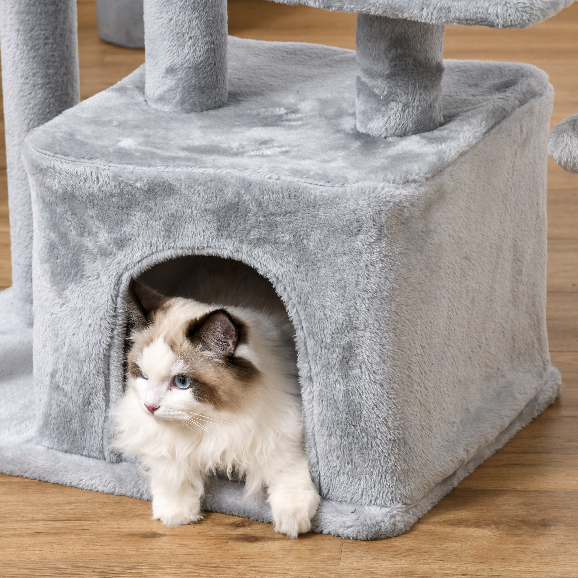 Un gato asomándose por una casita de árbol para gatos gris. El gato es blanco y gris.
