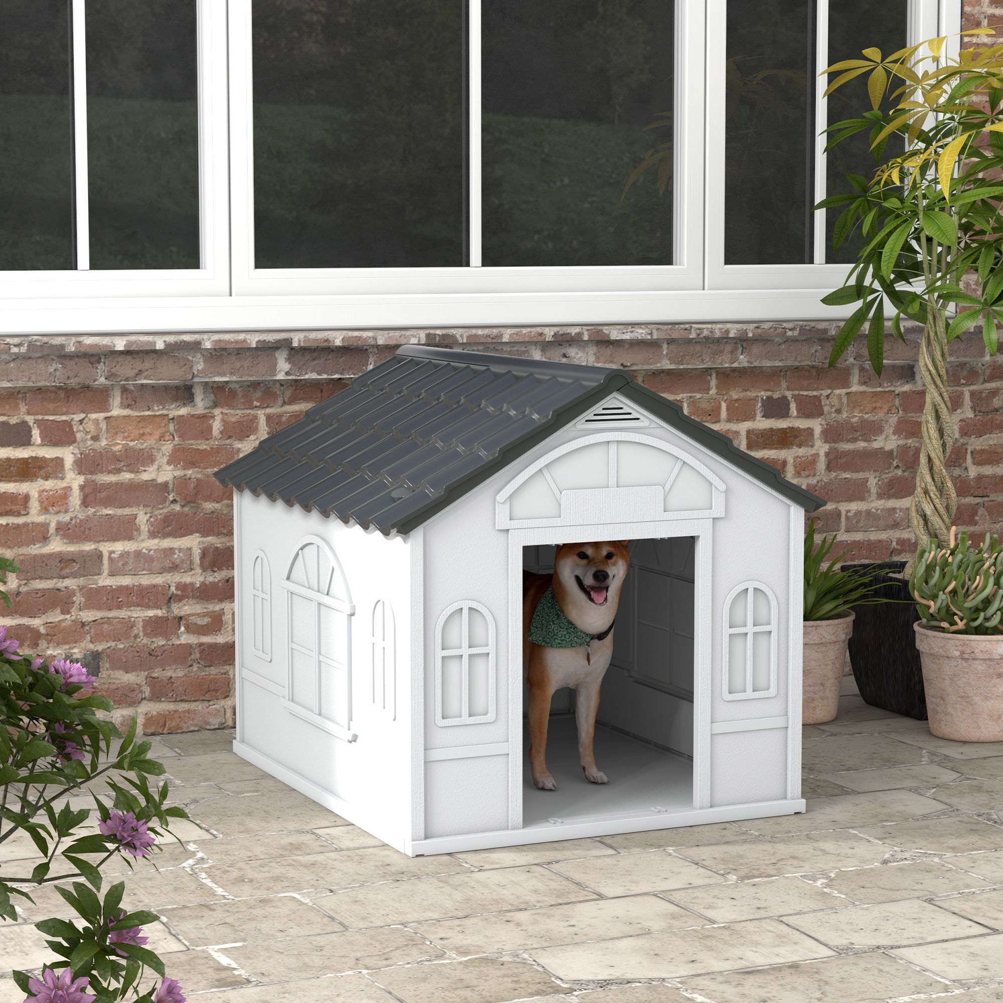 Casa para perros blanca con un perro dentro, colocada en un patio de ladrillo. Bufanda verde alrededor del cuello del perro.