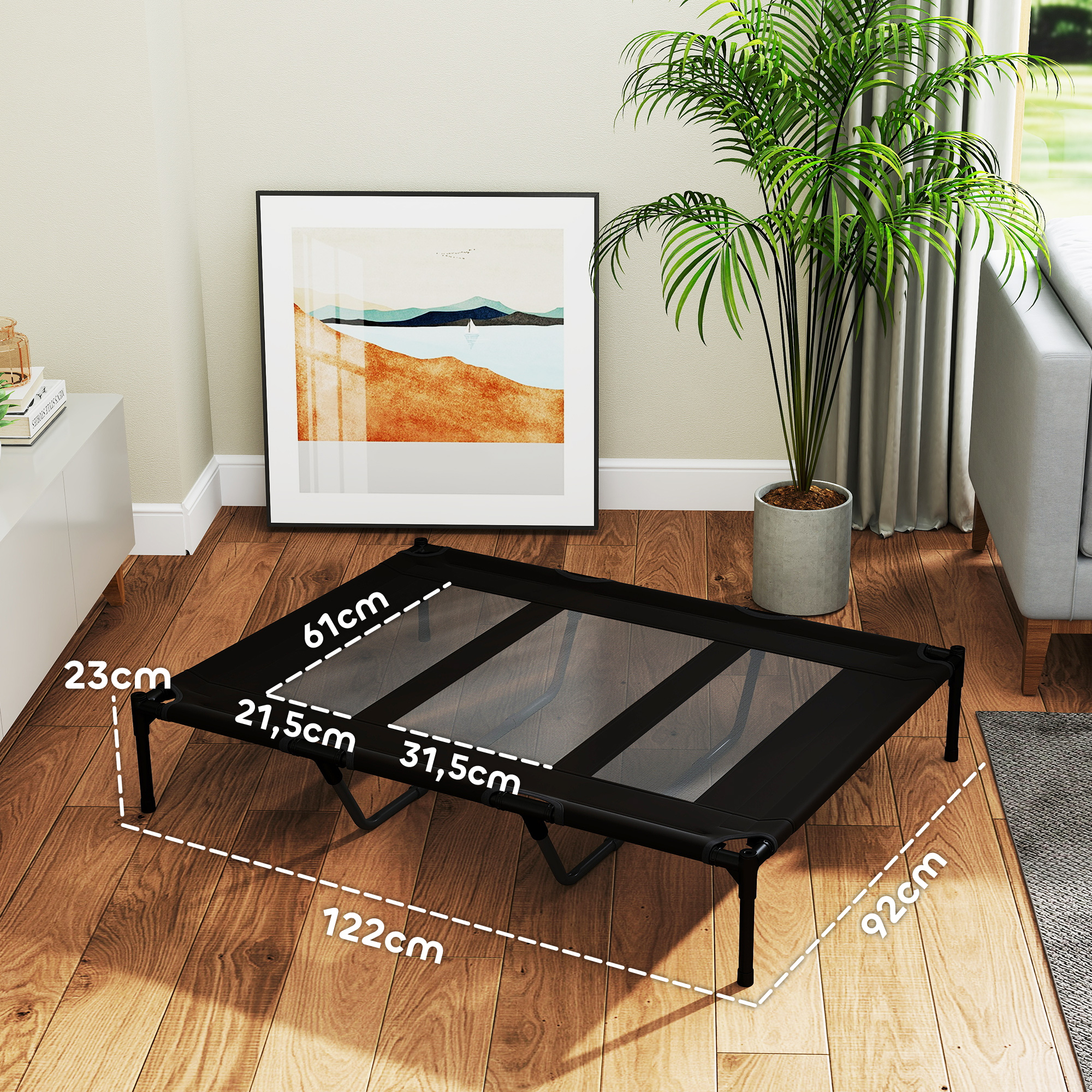 Una cama para perros negra con dimensiones se coloca en un piso de madera cerca de un sofá gris.