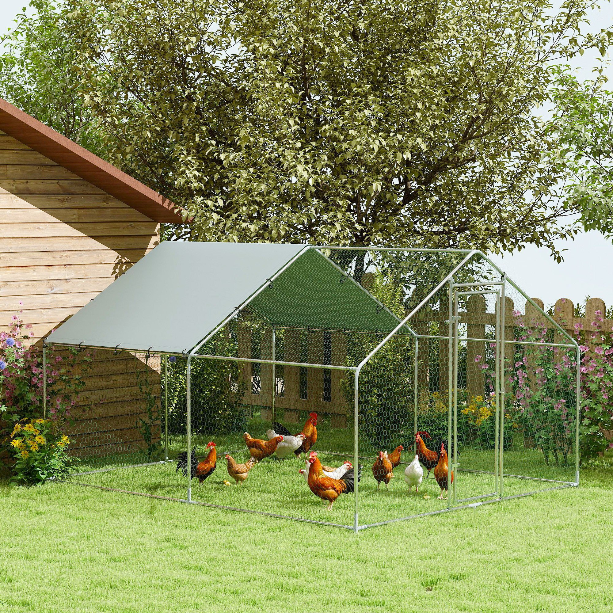 Un gallinero con gallinas dentro. Tiene un techo verde, paredes de malla de alambre y está en un jardín.