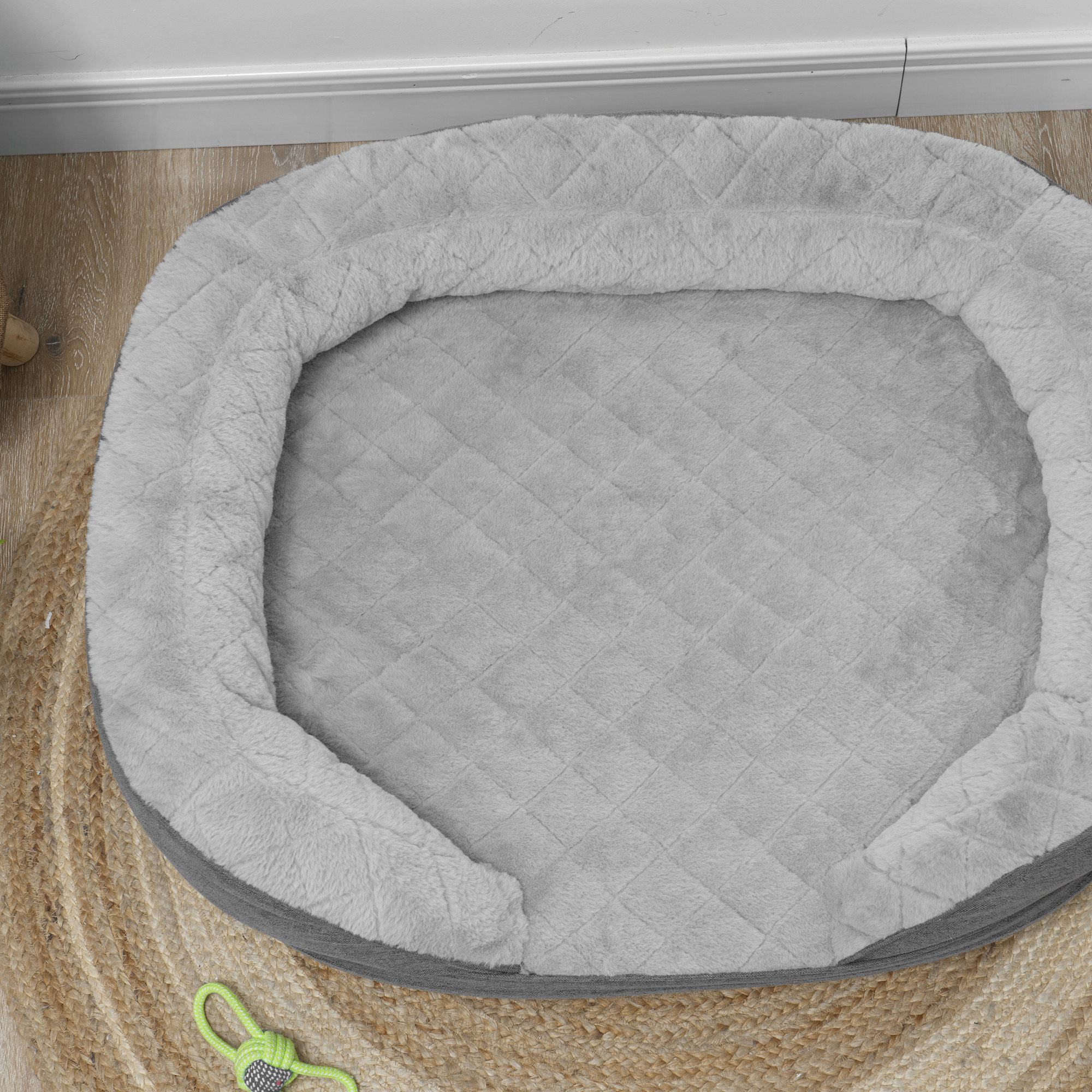 Cama gris para mascotas sobre una estera tejida. Juguete verde cerca.