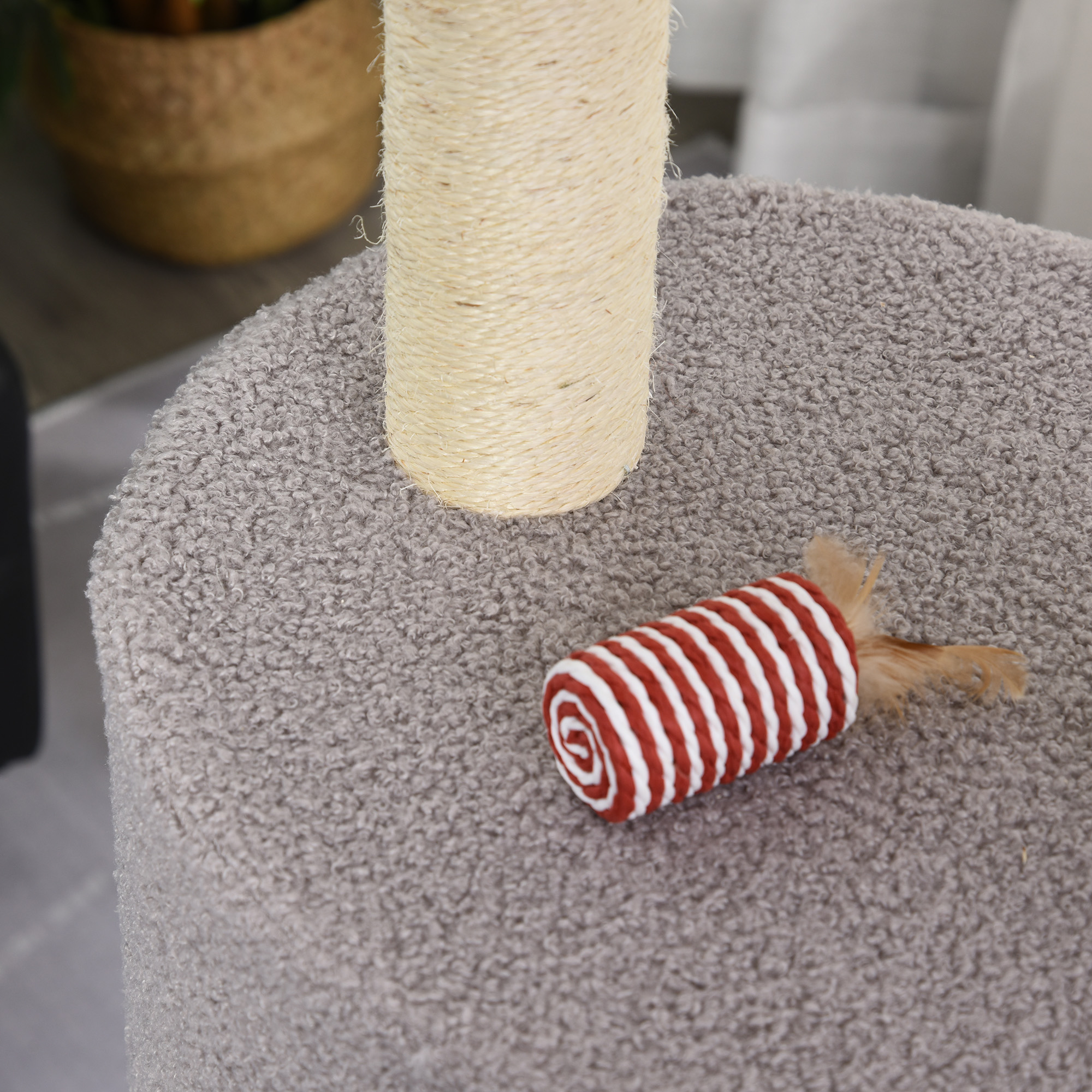 Un primer plano de un poste rascador para gatos. El poste rascador es beige con un juguete a rayas rojas y blancas.