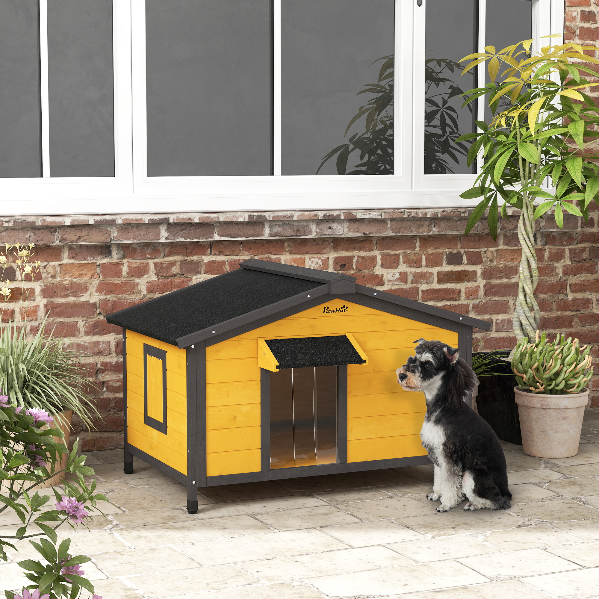 Una caseta para perros amarilla con techo negro, y un perro sentado afuera en un jardín.