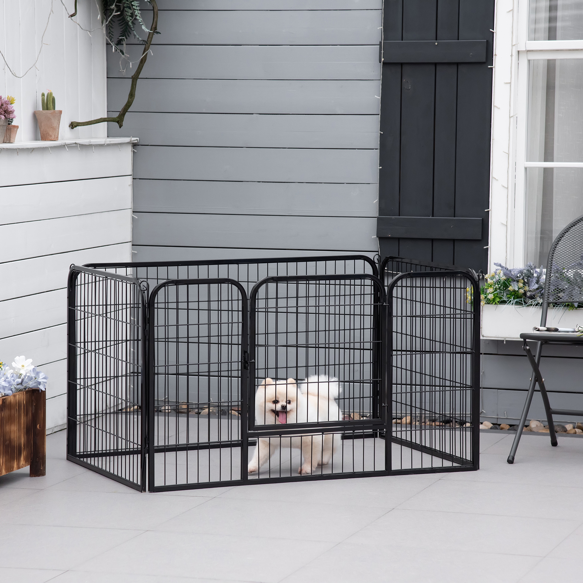 Un corral de metal negro está en un patio con un perro dentro. Una cerca es visible en el fondo.