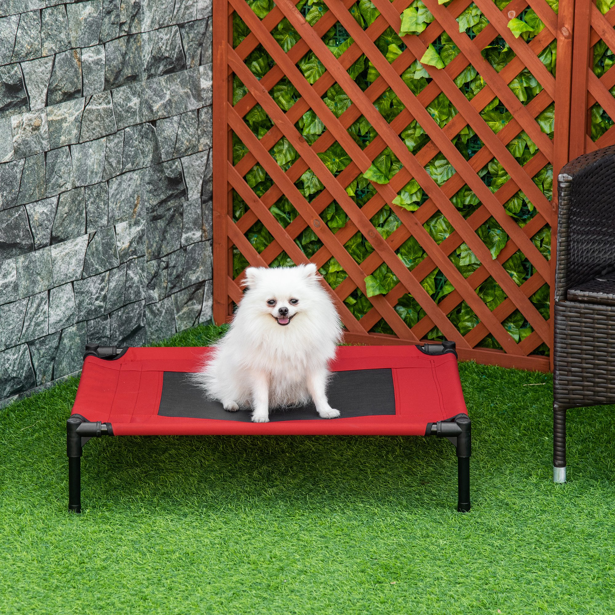 Un perro blanco en una cama para perros roja sobre hierba en un jardín.