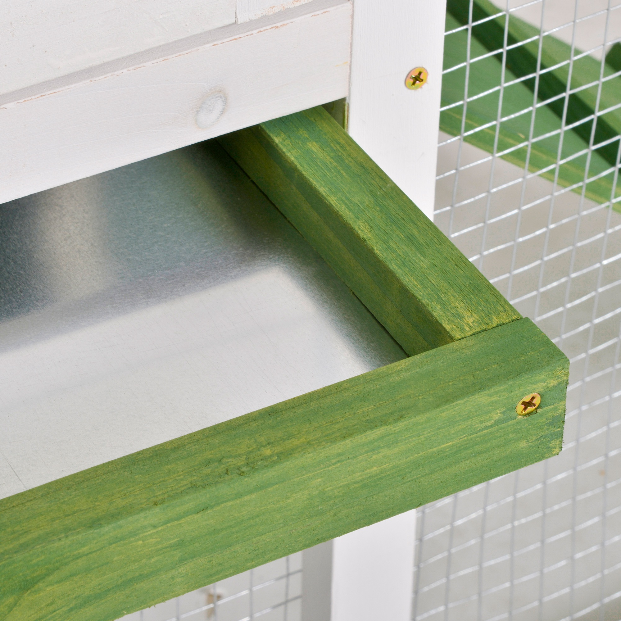 Un cajón verde de una jaula está abierto. El cajón tiene un fondo de metal.
