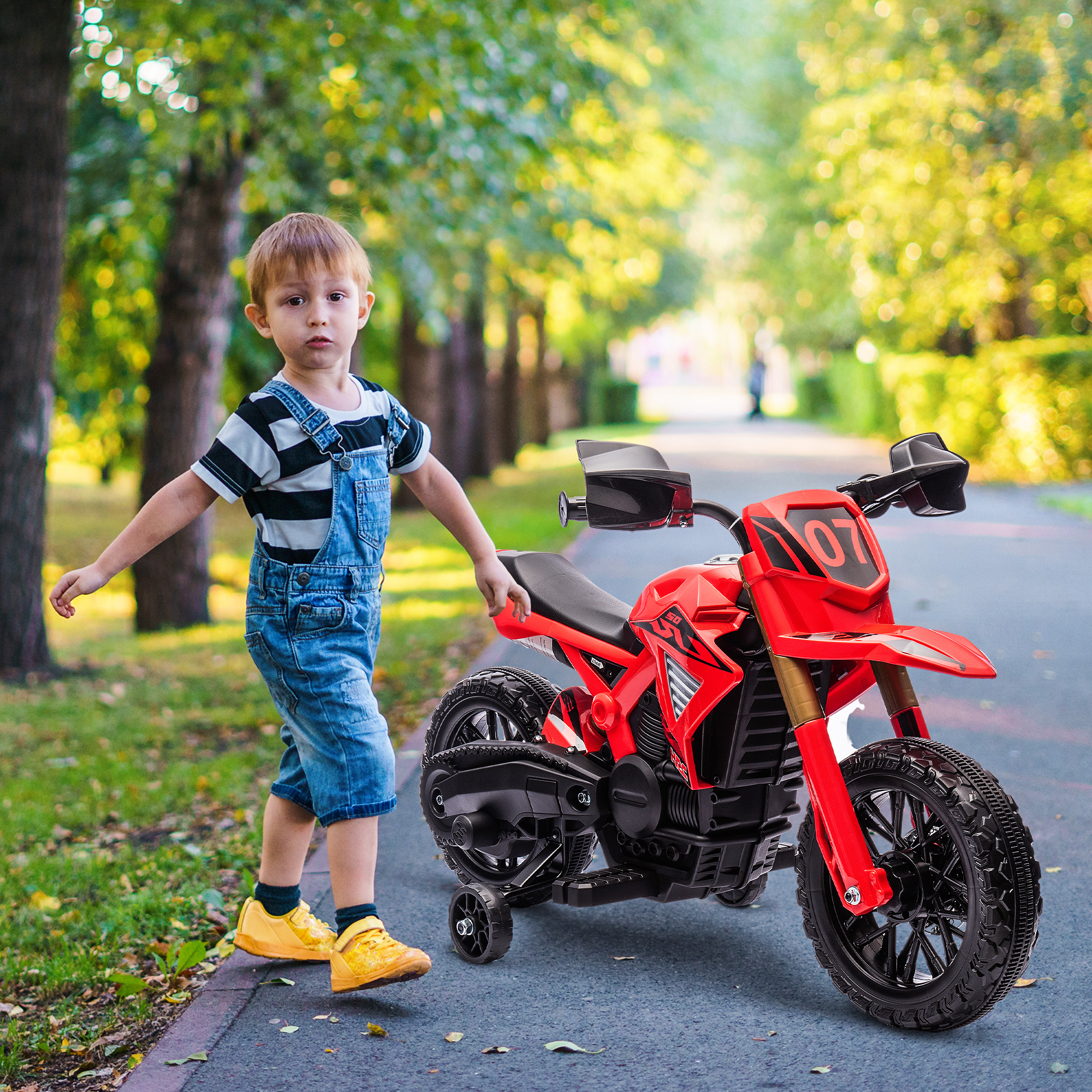 Un niño de pie junto a un juguete de motocicleta roja. El fondo es una carretera y árboles.