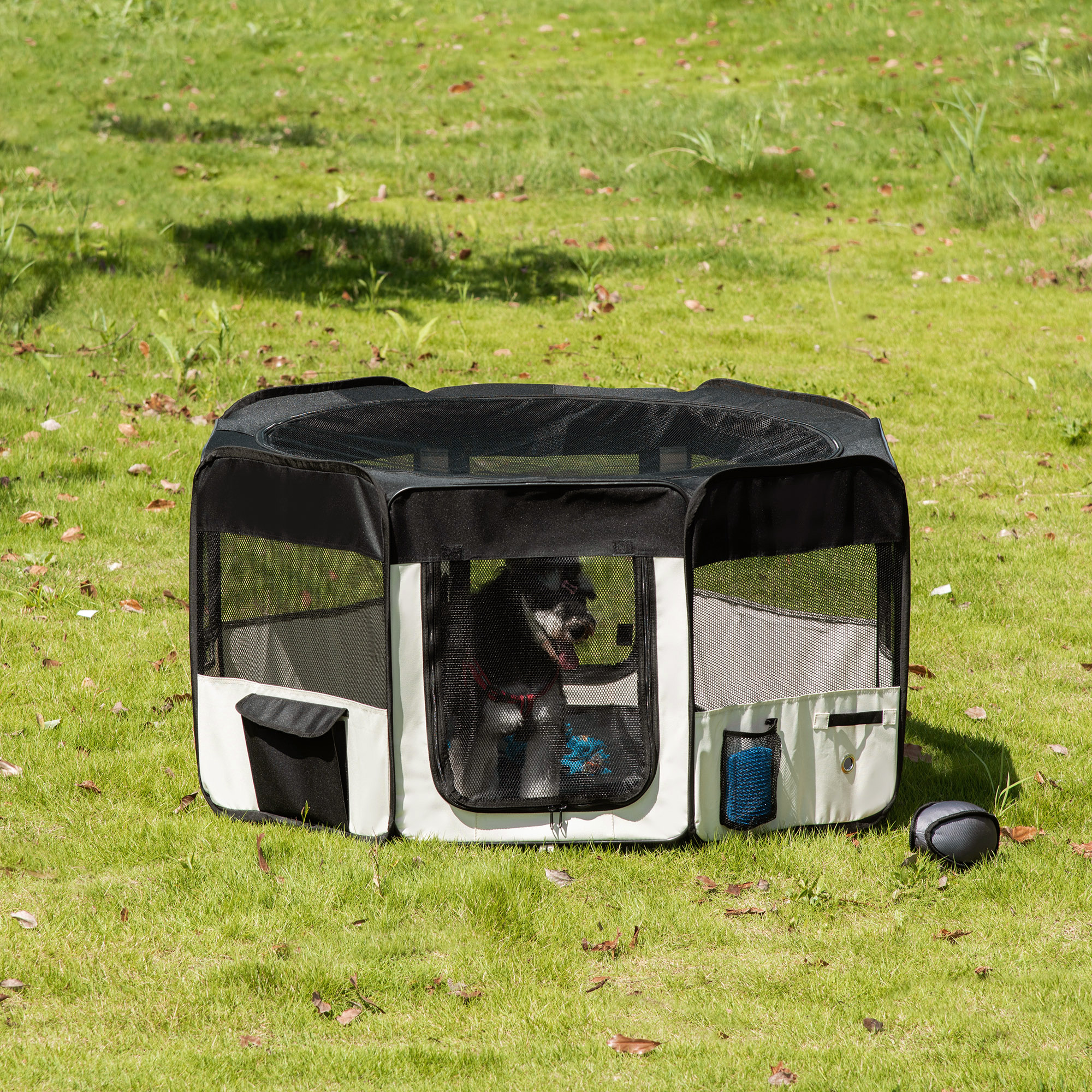 Un parque para mascotas en blanco y negro sobre hierba. Un perro está dentro del parque, hay una pelota en la hierba.