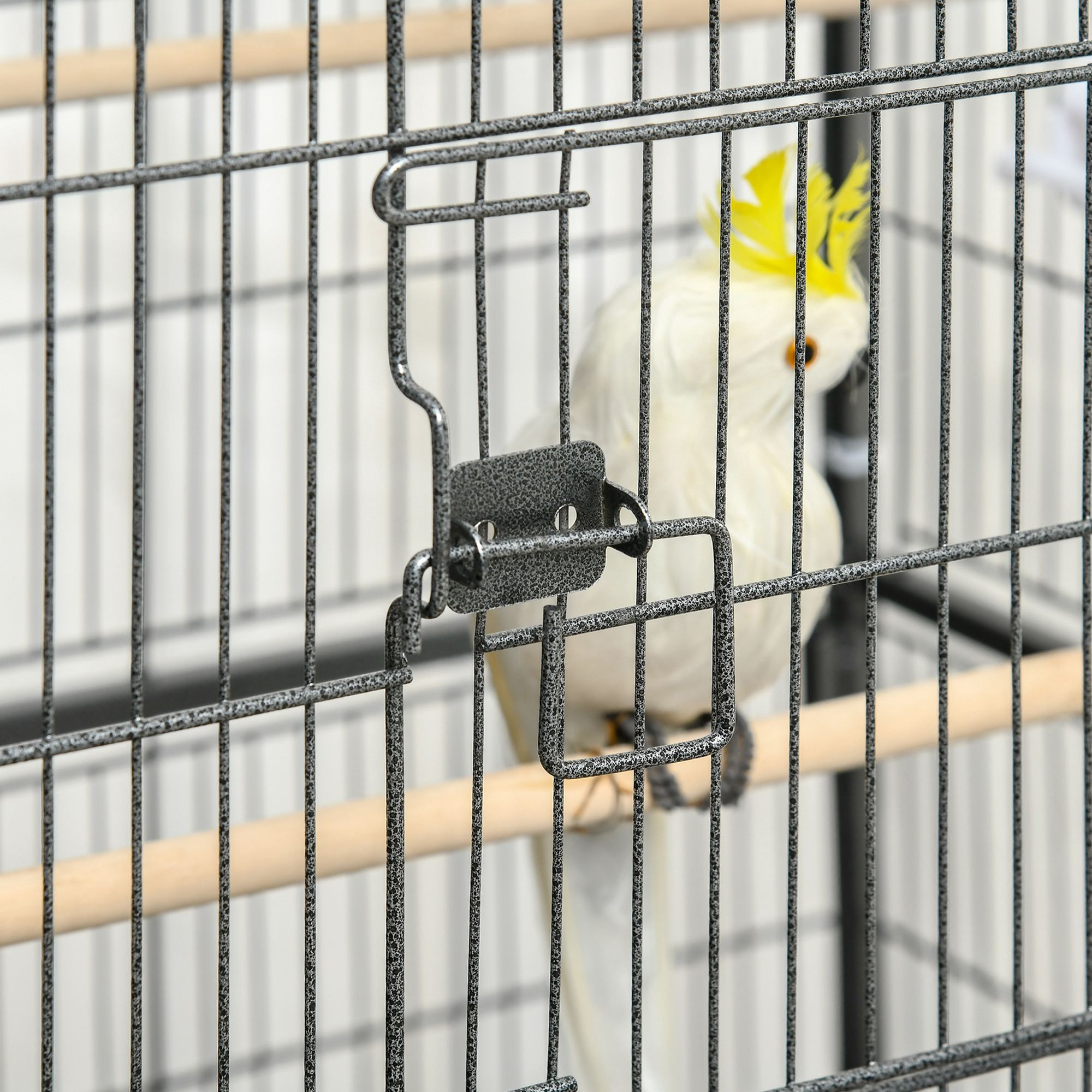 Una cacatúa blanca dentro de una jaula de metal. Está posado en un pasador de madera.