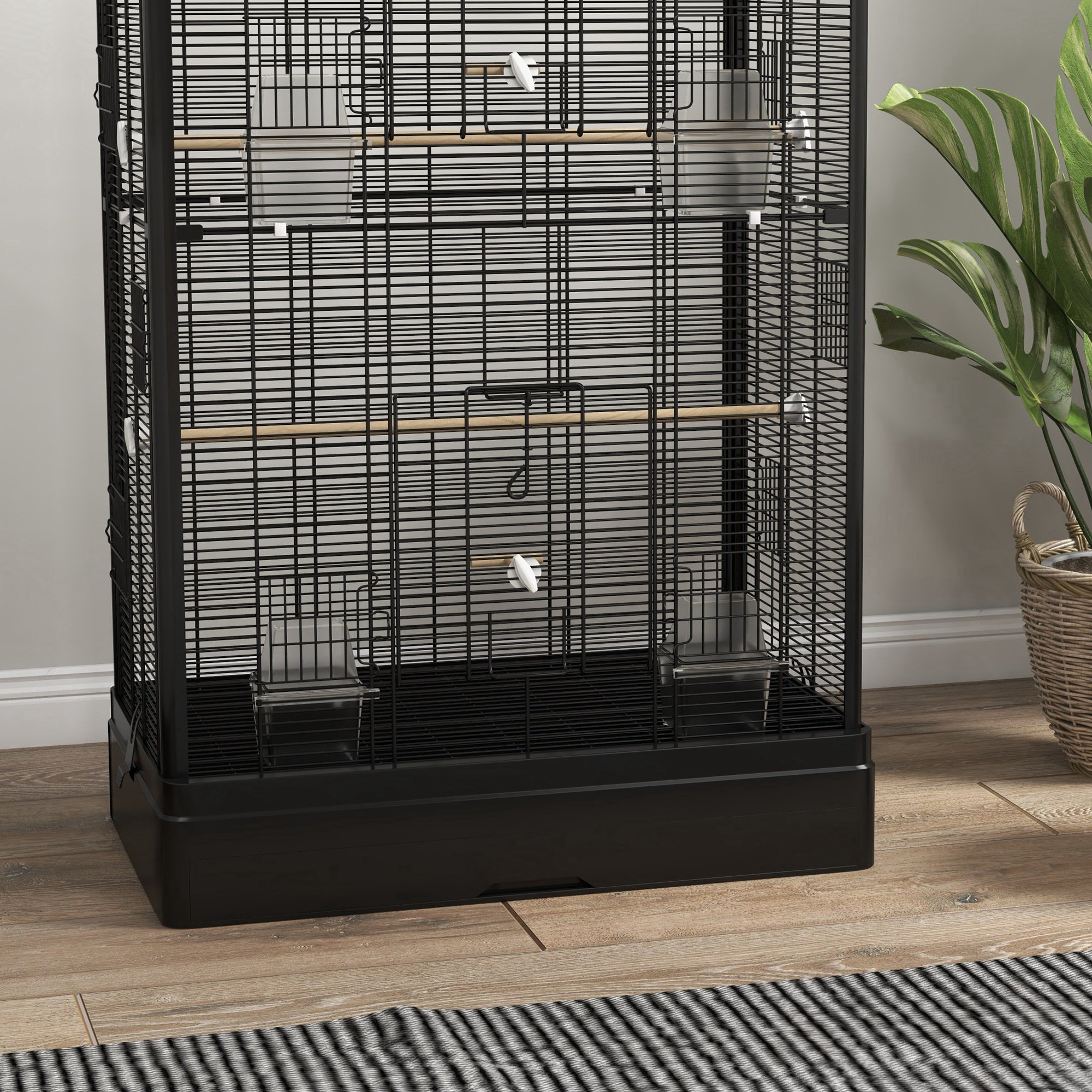 Una jaula negra para pájaros con base negra, perchas de madera y accesorios.