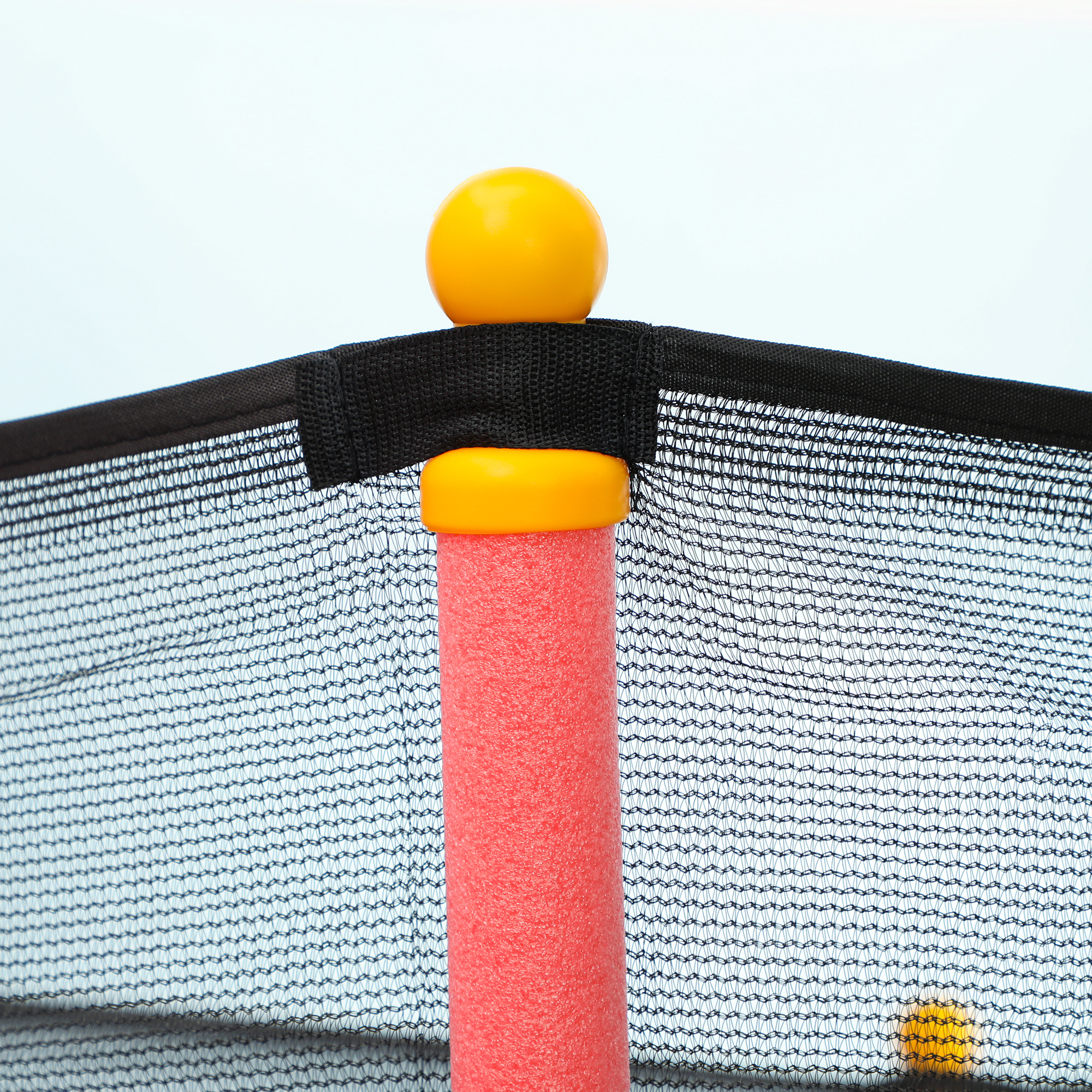 Primo piano di una rete di sicurezza per trampolino con una palla gialla in cima a un palo rosso.
