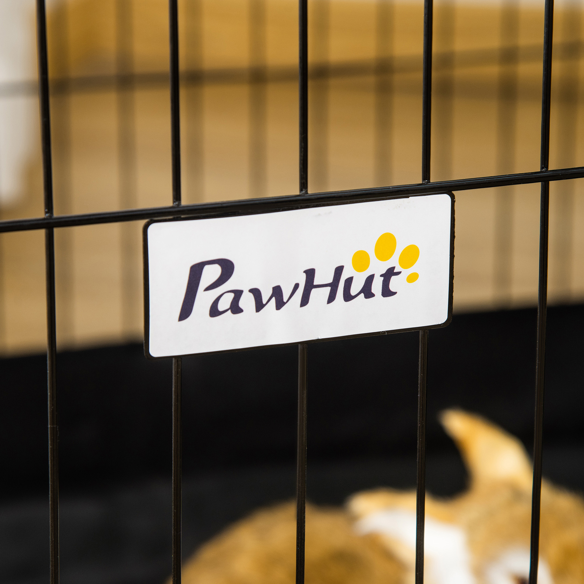 Primer plano de un letrero de PawHut en una jaula para perros de alambre negro. Perro borroso.