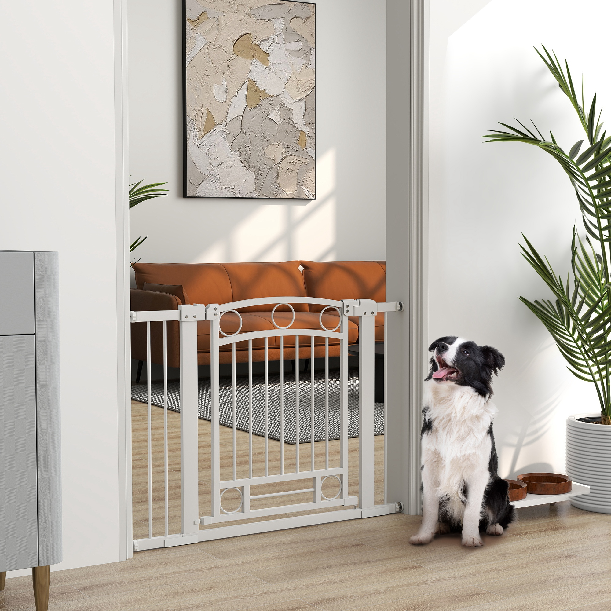 Un perro está sentado cerca de una barrera blanca para bebés. El perro es blanco y negro, con la lengua fuera. Salón en el fondo.