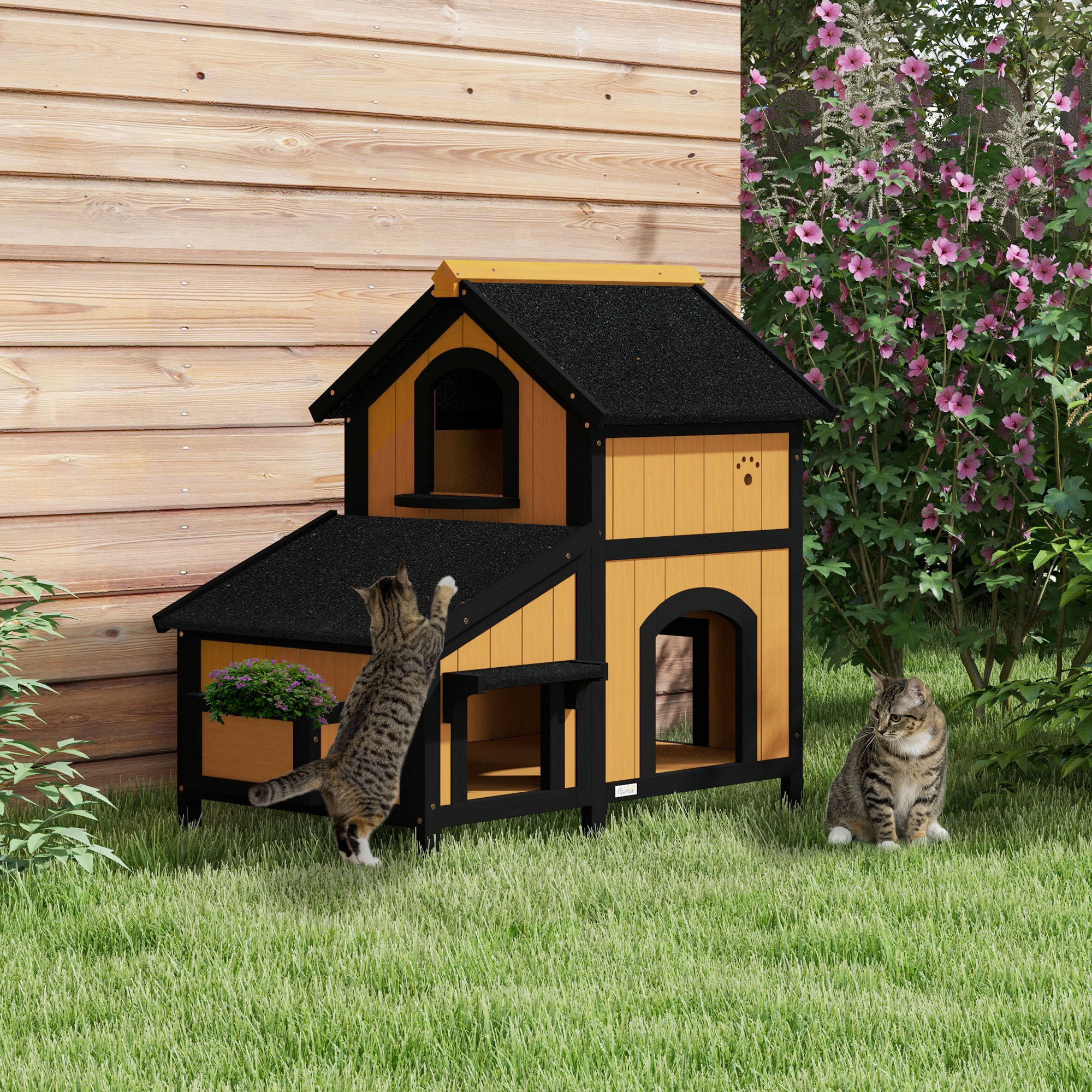 Casa para gatos de dos niveles. Gatos jugando cerca. La casa tiene un diseño negro y amarillo.
