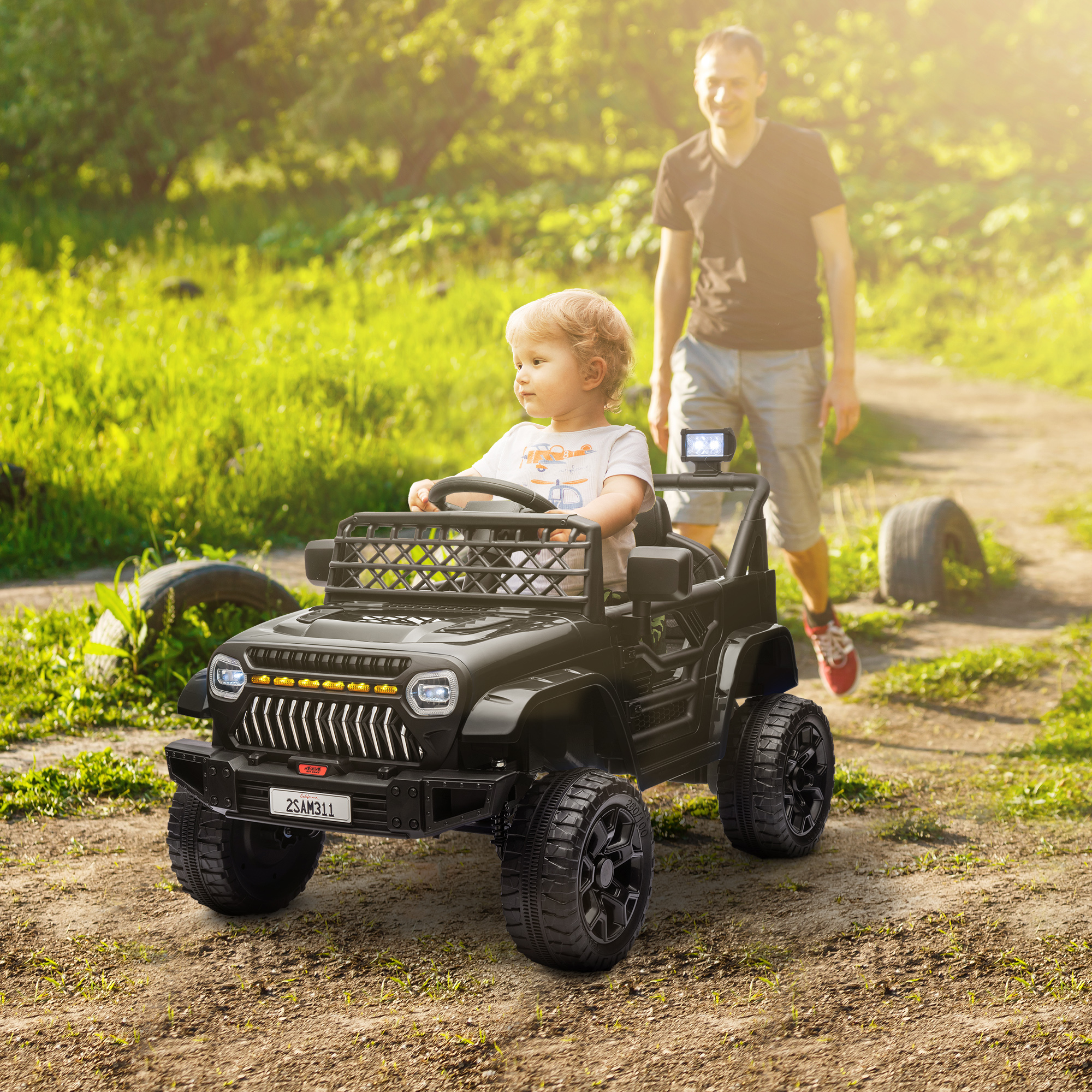 Un niño en un jeep de juguete negro, conducido por un camino de tierra, con un hombre caminando detrás, en un día soleado.