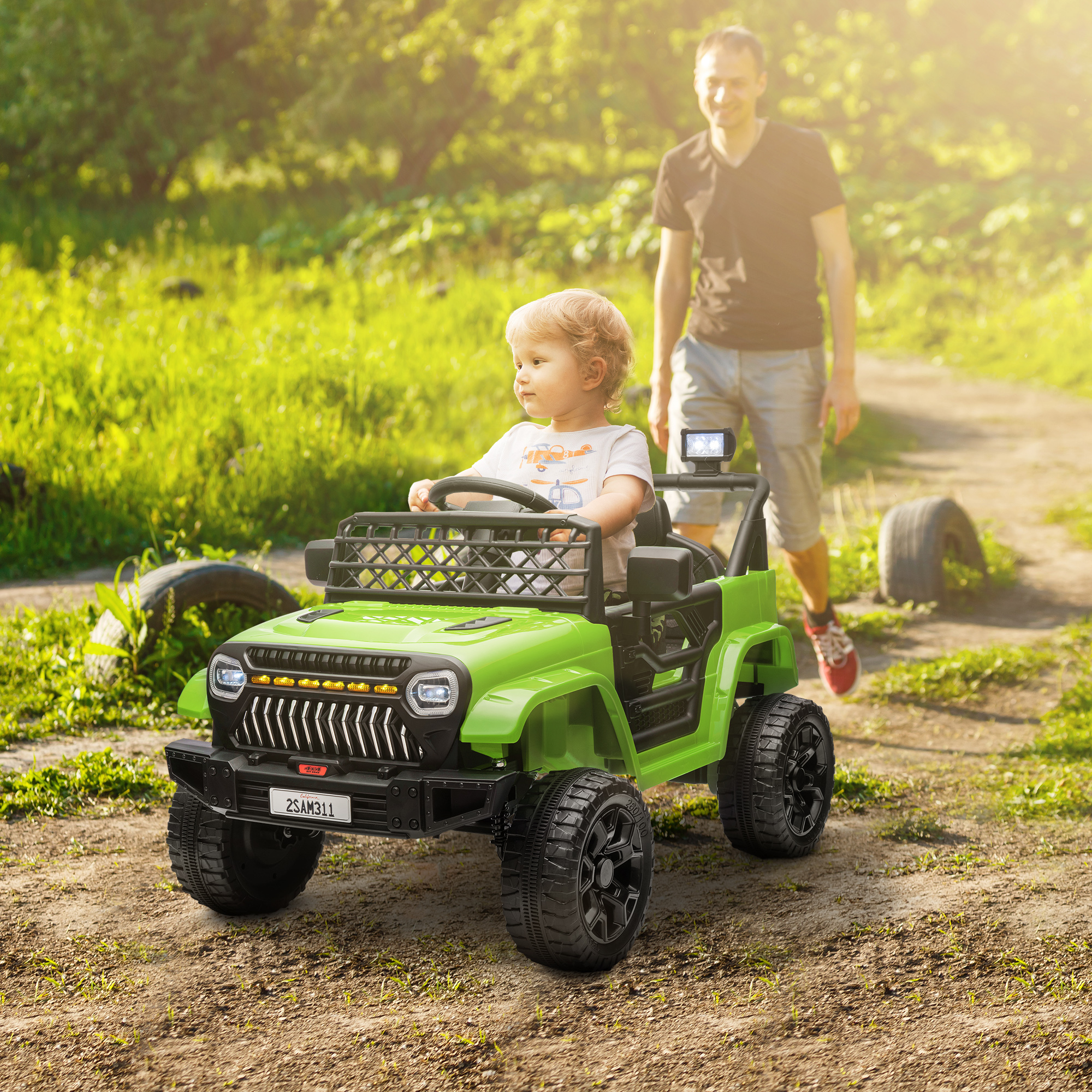 Un niño conduce un jeep de juguete verde por un camino de tierra, con un adulto caminando detrás.