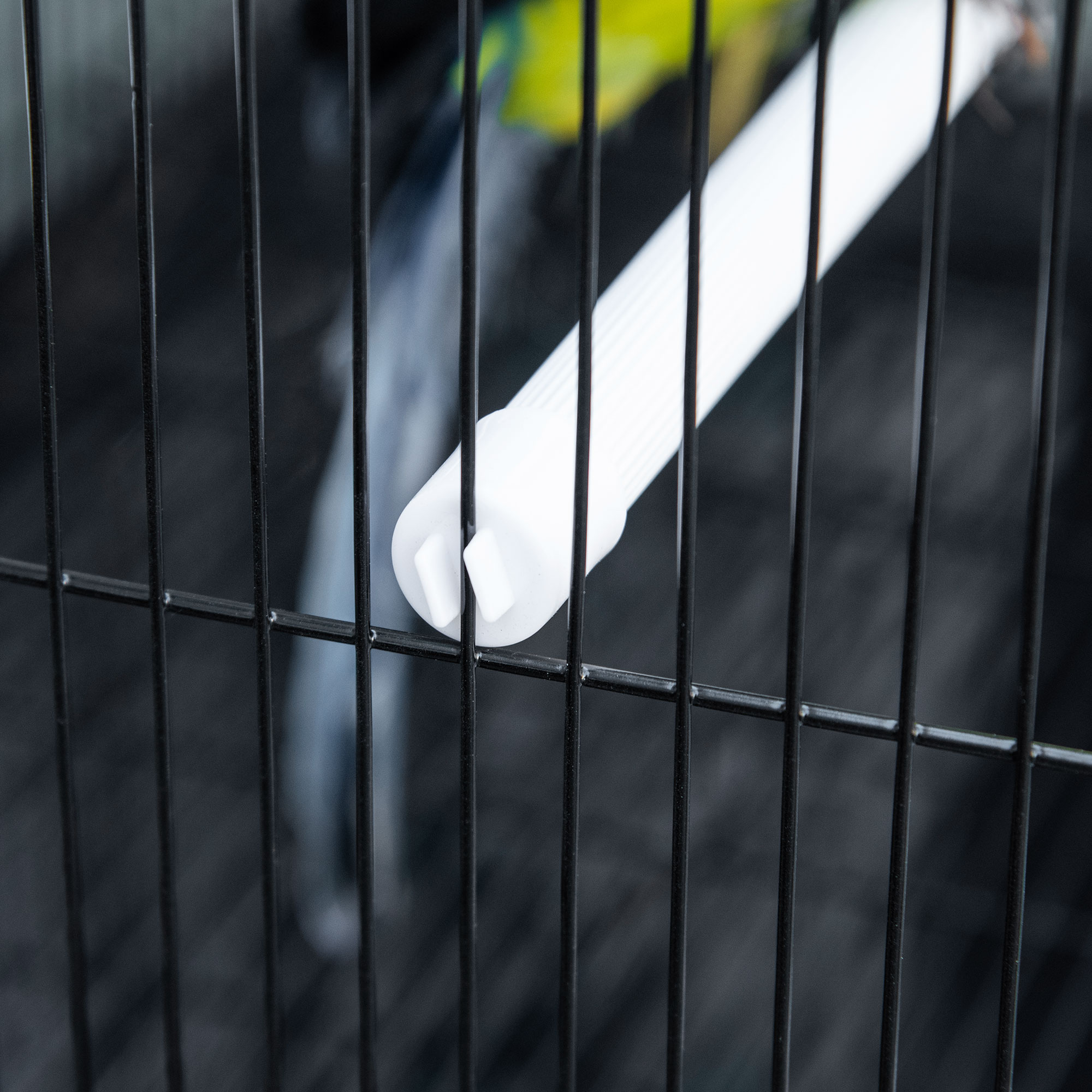 Primer plano de una percha de plástico blanco para pájaros dentro de una jaula de alambre negro con fondo oscuro.