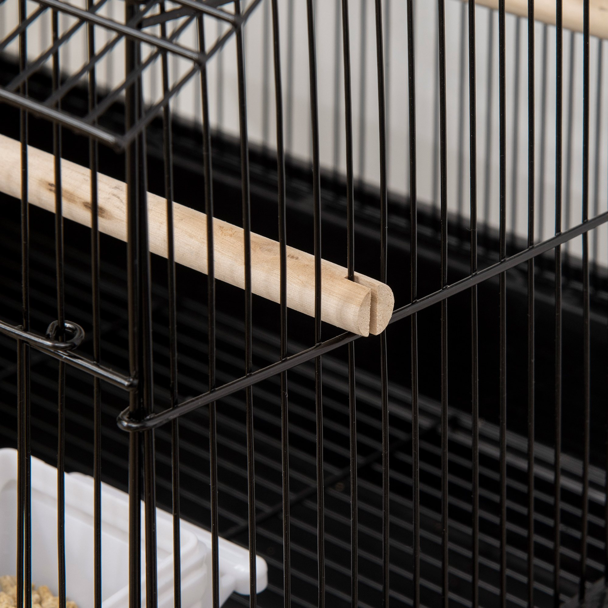 Primer plano de una percha de madera dentro de una jaula negra.