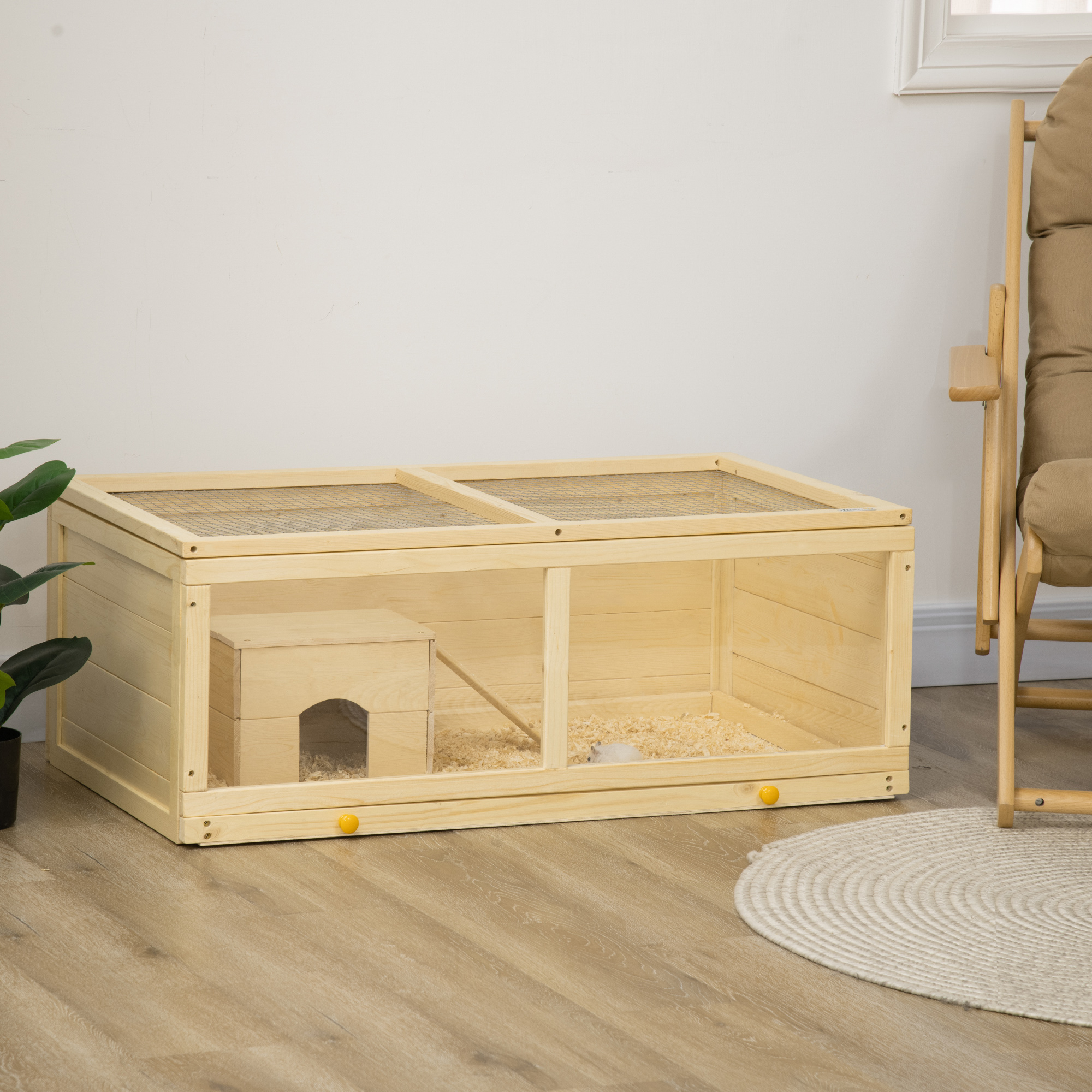 Recinto de madera para mascotas. Cuenta con una casita, lecho y un hámster. La habitación tiene suelo de madera y una silla.