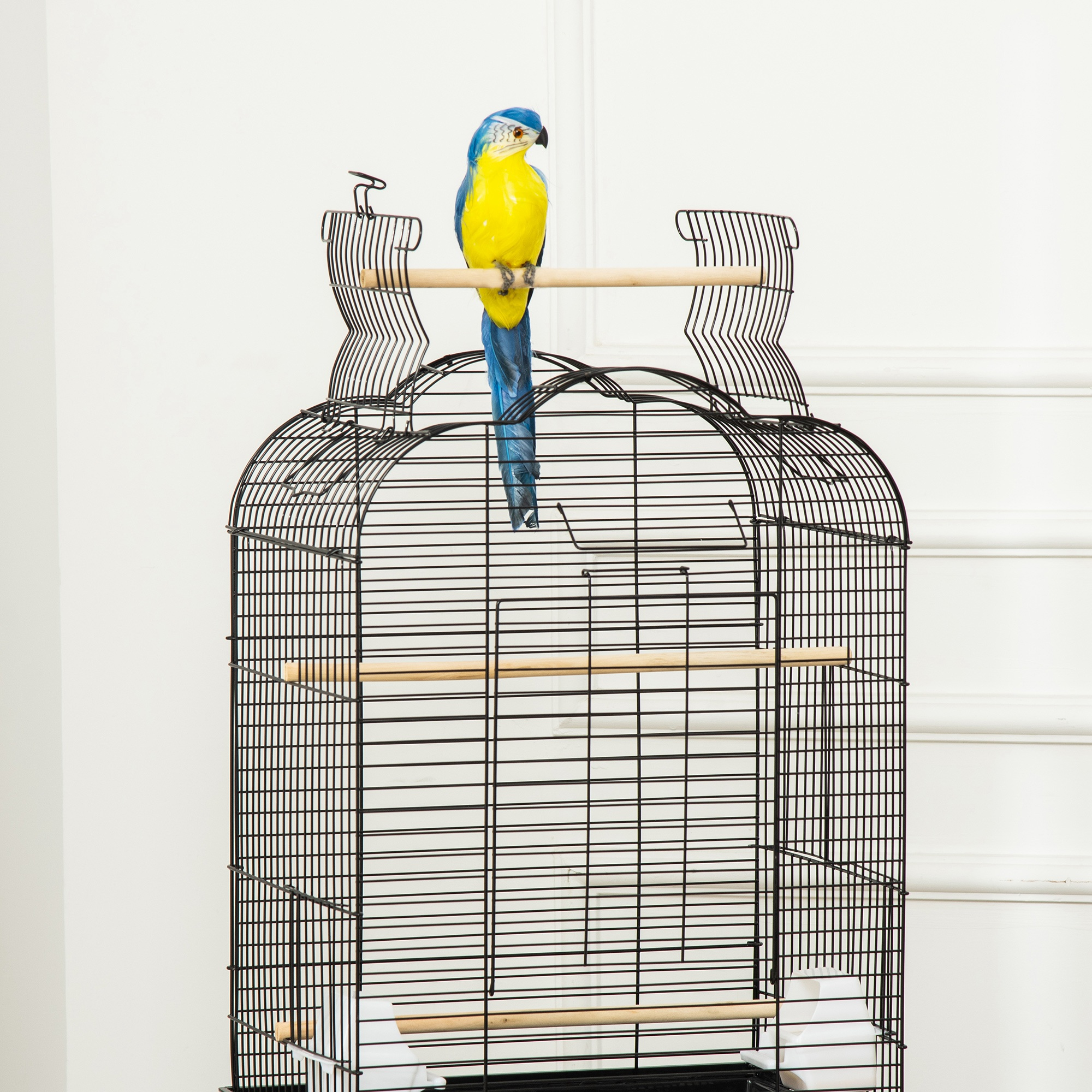 Jaula negra para pájaros con un loro azul y amarillo posado en una percha de madera. Está en una habitación.