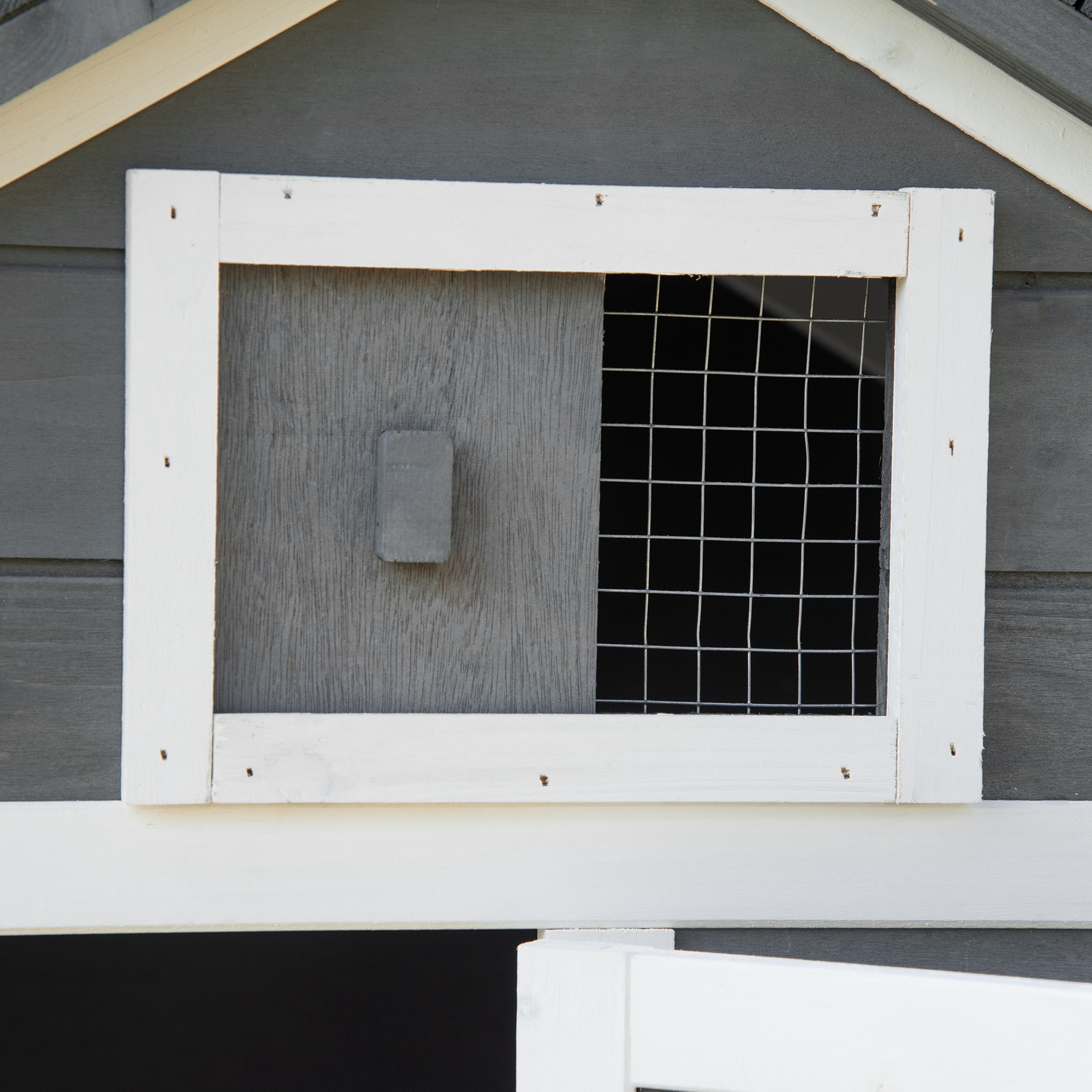 Primer plano de una ventana de casa para mascotas. Marco gris con panel de madera y malla de alambre. Exterior blanco.
