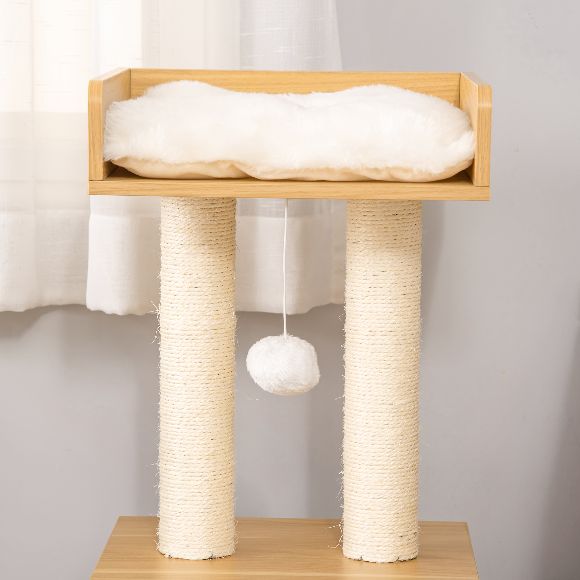 Un árbol para gatos con una cama esponjosa en la parte superior. Dos postes con cuerda y una bola colgante. Base de madera.