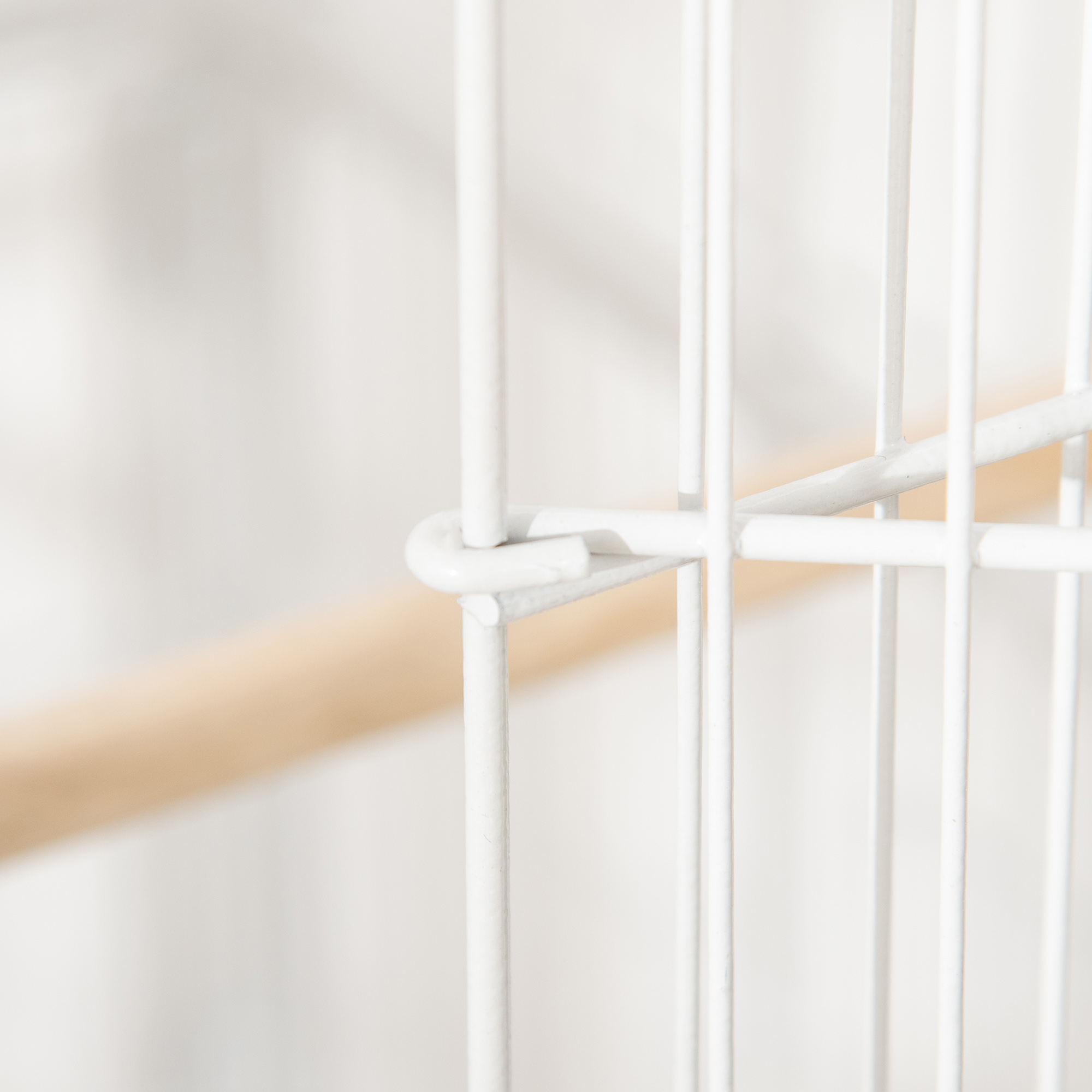 Primer plano de una jaula de metal blanco, que muestra la intersección de las barras y una percha de madera.