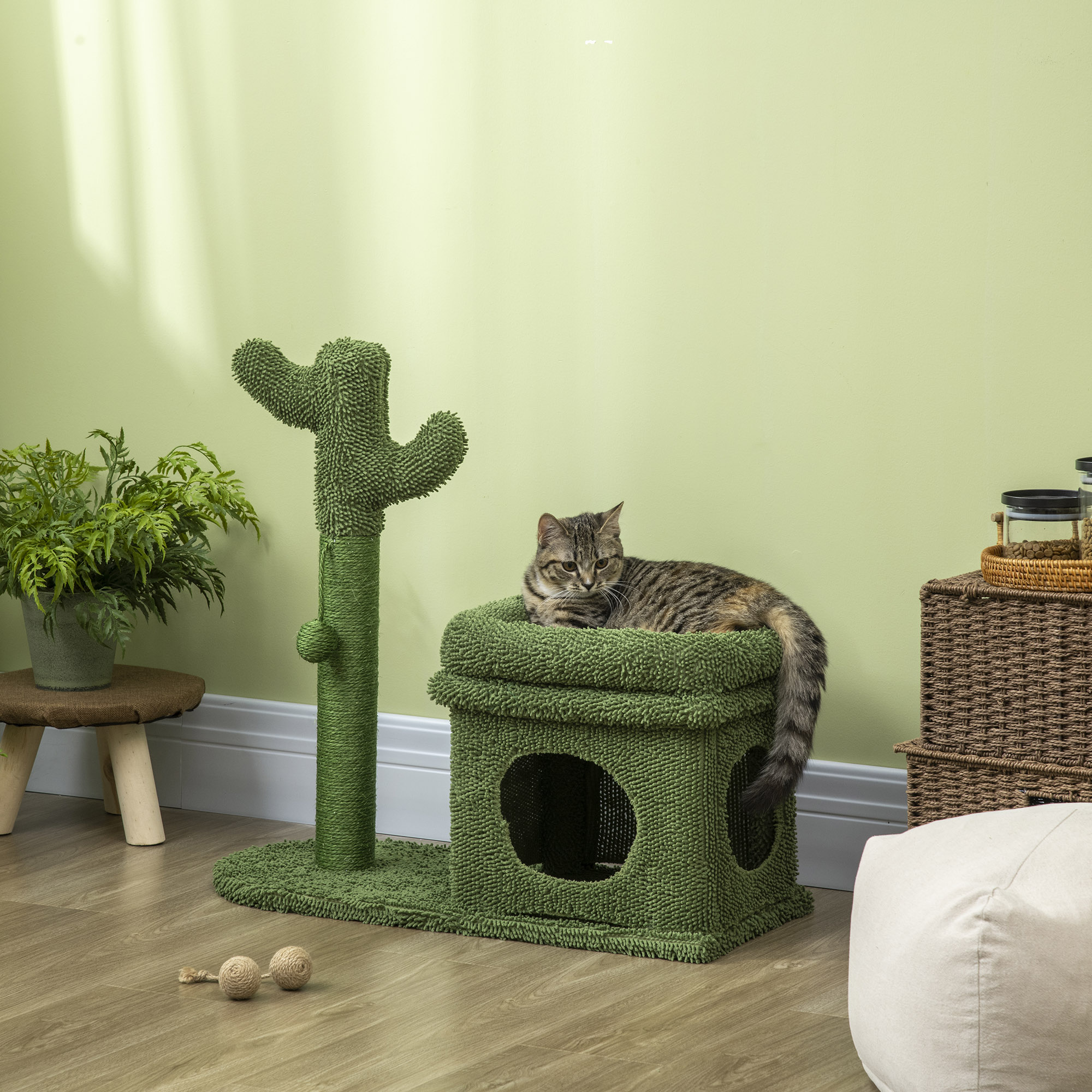 Un gato en un árbol para gatos verde en forma de cactus. Hay bolas y una planta cerca del árbol.