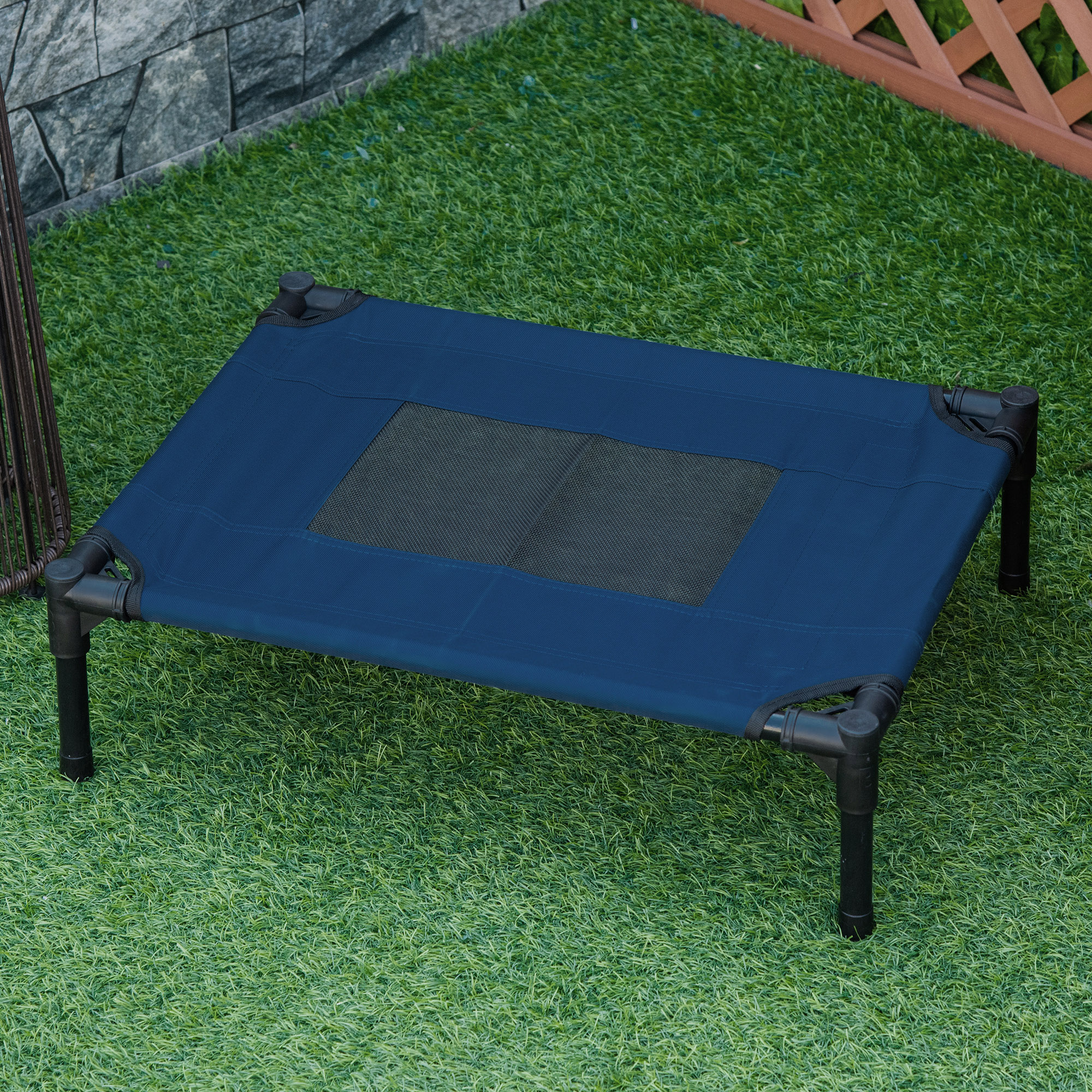 Cama elevada azul para mascotas sobre hierba verde. Cuenta con un marco negro y un centro de malla.