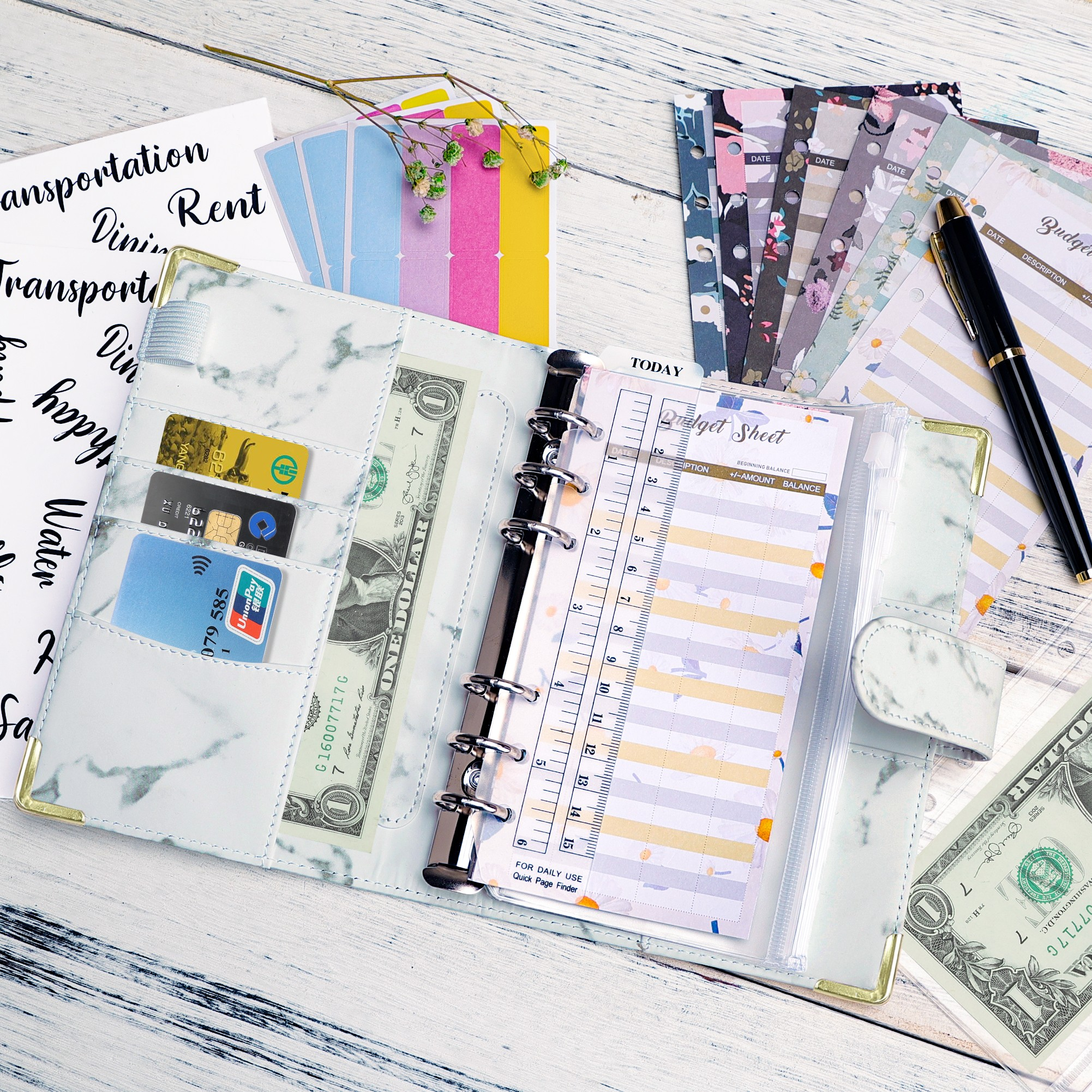 Ein Planer mit Geld, Karten und Budgettabellen. Ein Stift liegt auf den Seiten mit floralen Designs.
