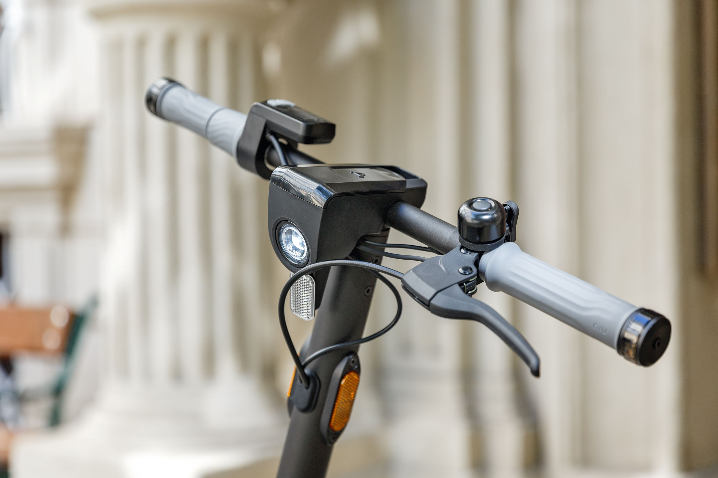 Primer plano del manillar de un scooter negro. Tiene una campana, luz y palanca de freno.