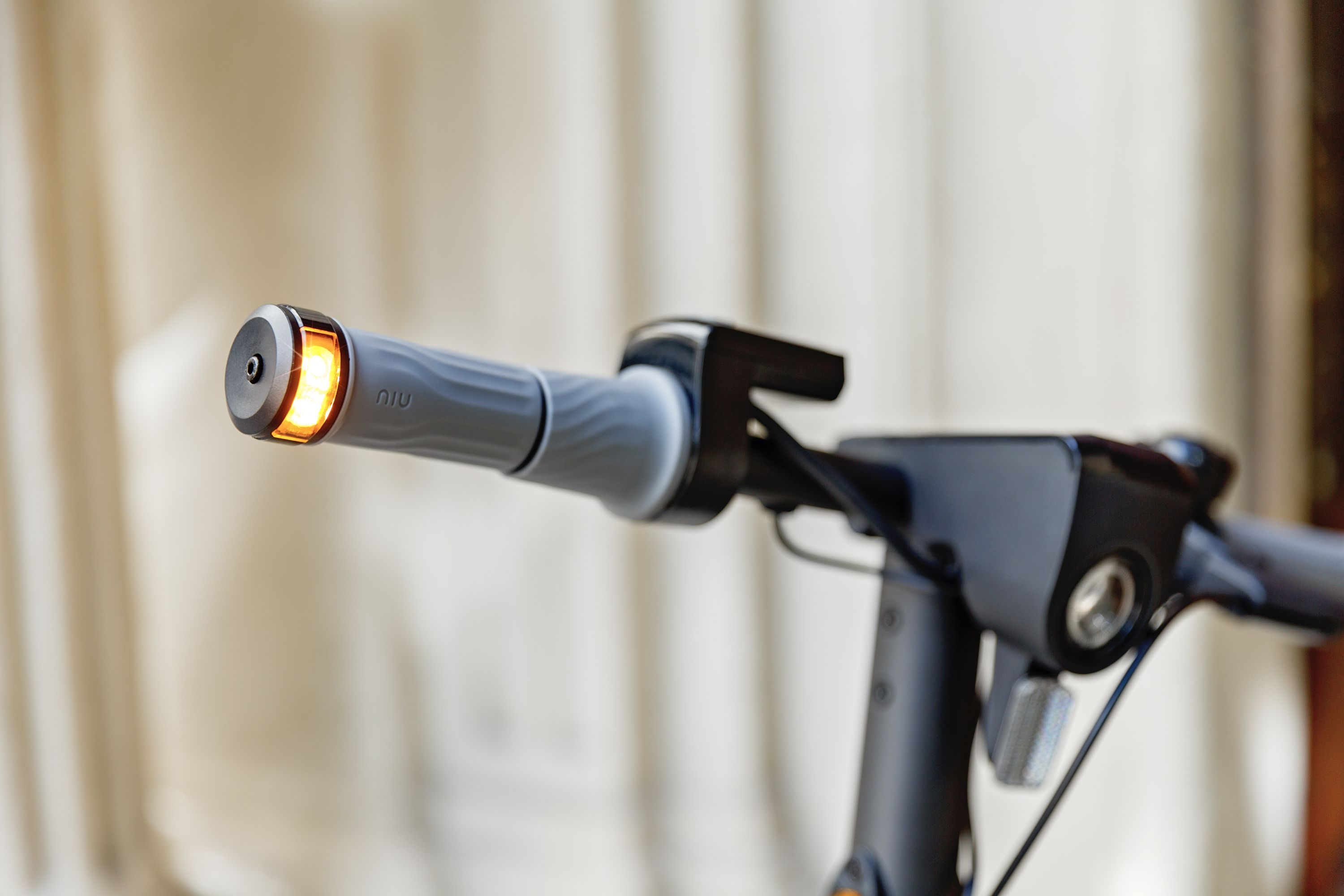 Primer plano del manillar de un scooter con empuñadura gris y luz de intermitente naranja.