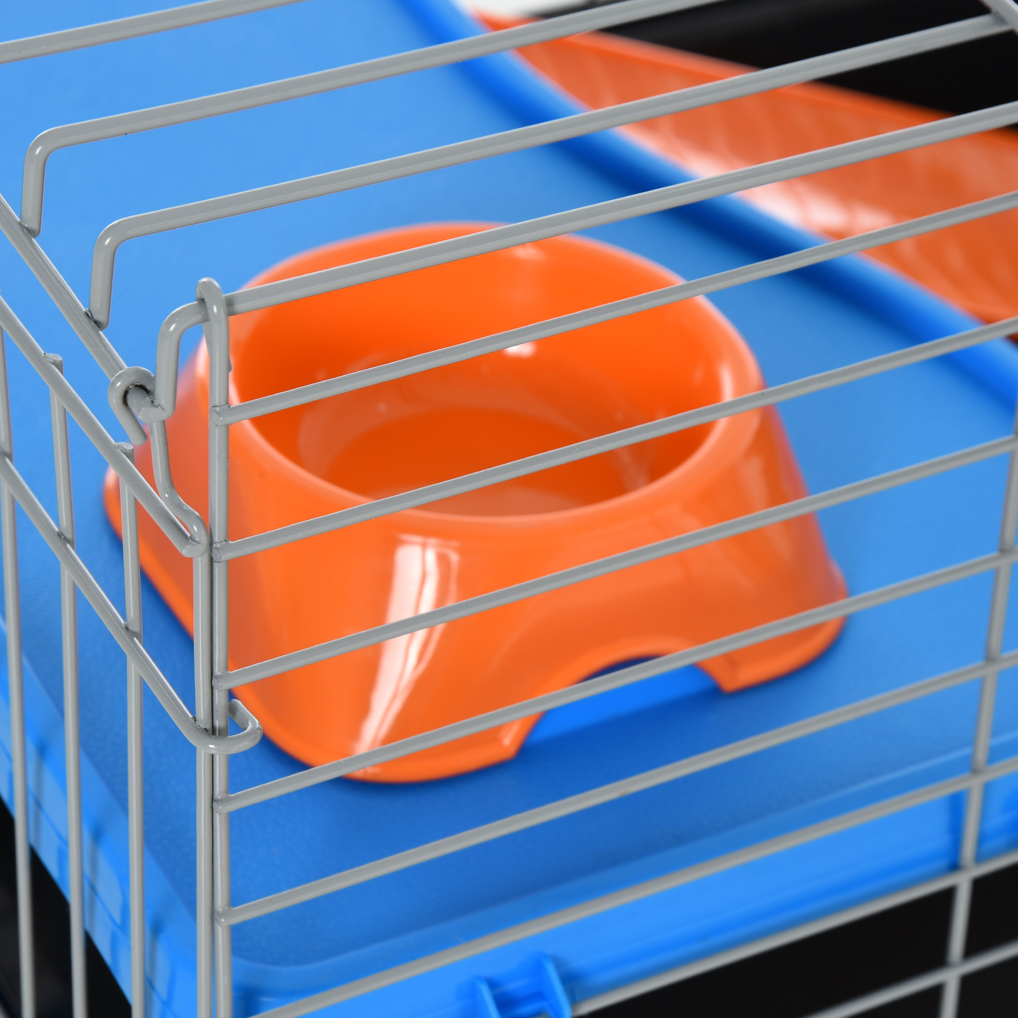 Una jaula de metal con un cuenco naranja en su interior, sobre una base azul, adecuada para mascotas pequeñas.