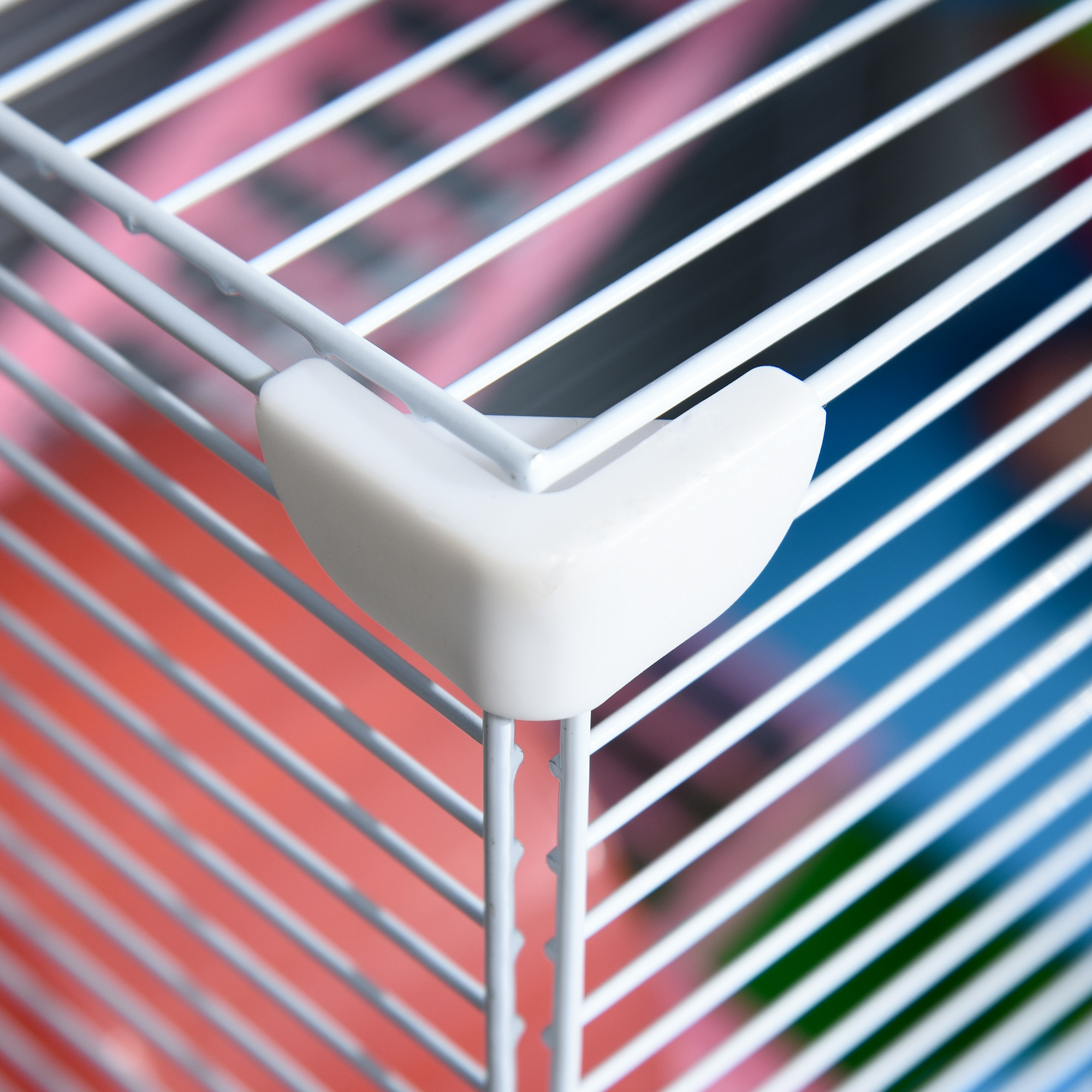 Primer plano de un protector de esquina de plástico blanco en una jaula de metal. Barras blancas sobre rosa y azul.