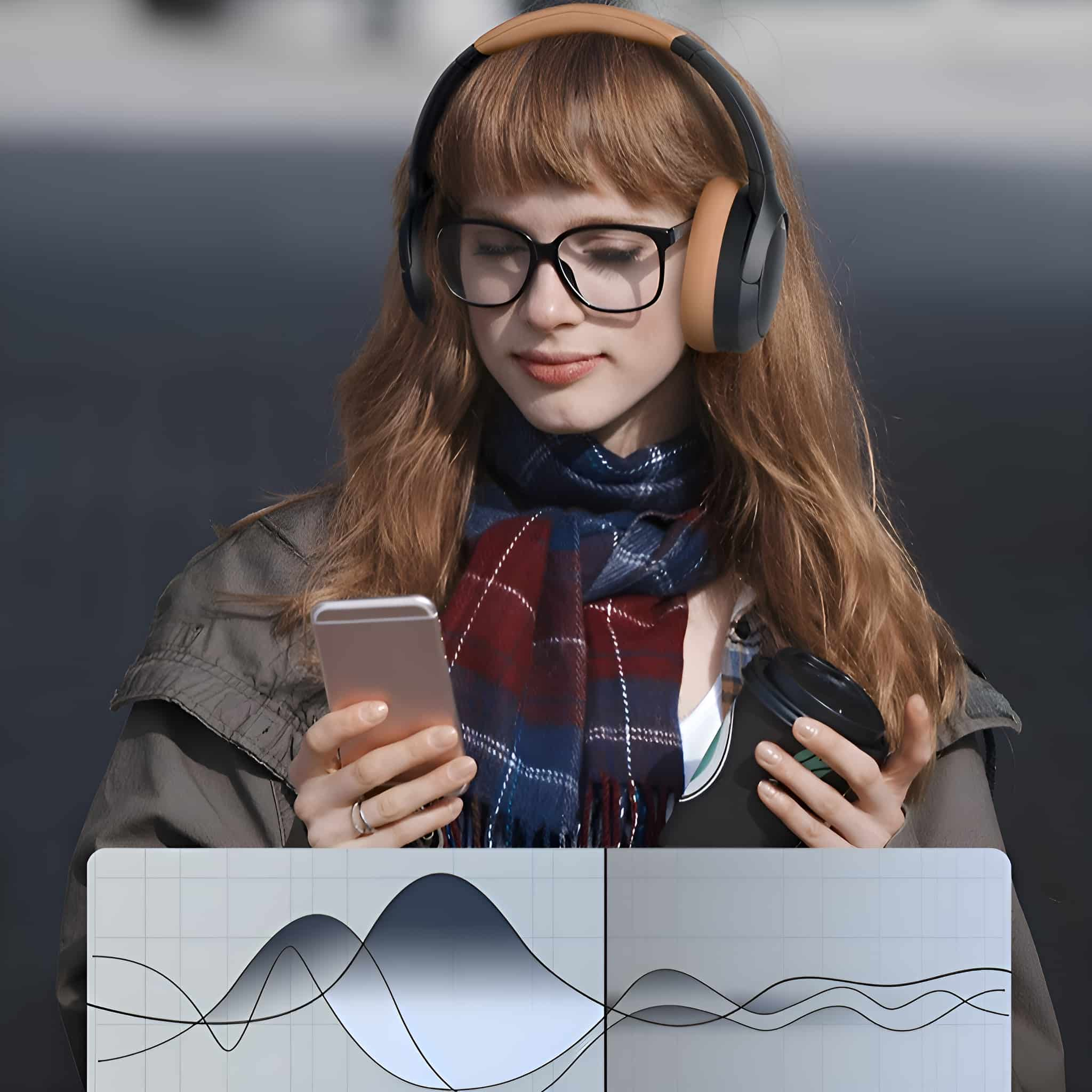 Eine Frau mit Kopfhörern und Brille, die ein Telefon und eine Tasse Kaffee hält.