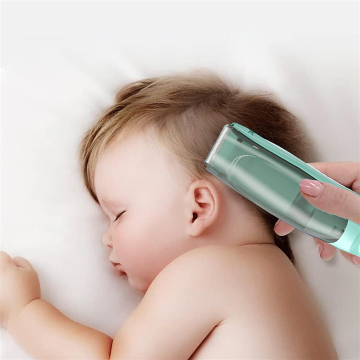 Ein Baby schläft, während eine Person einen grünen Haarschneider an der Seite des Babykopfes verwendet.