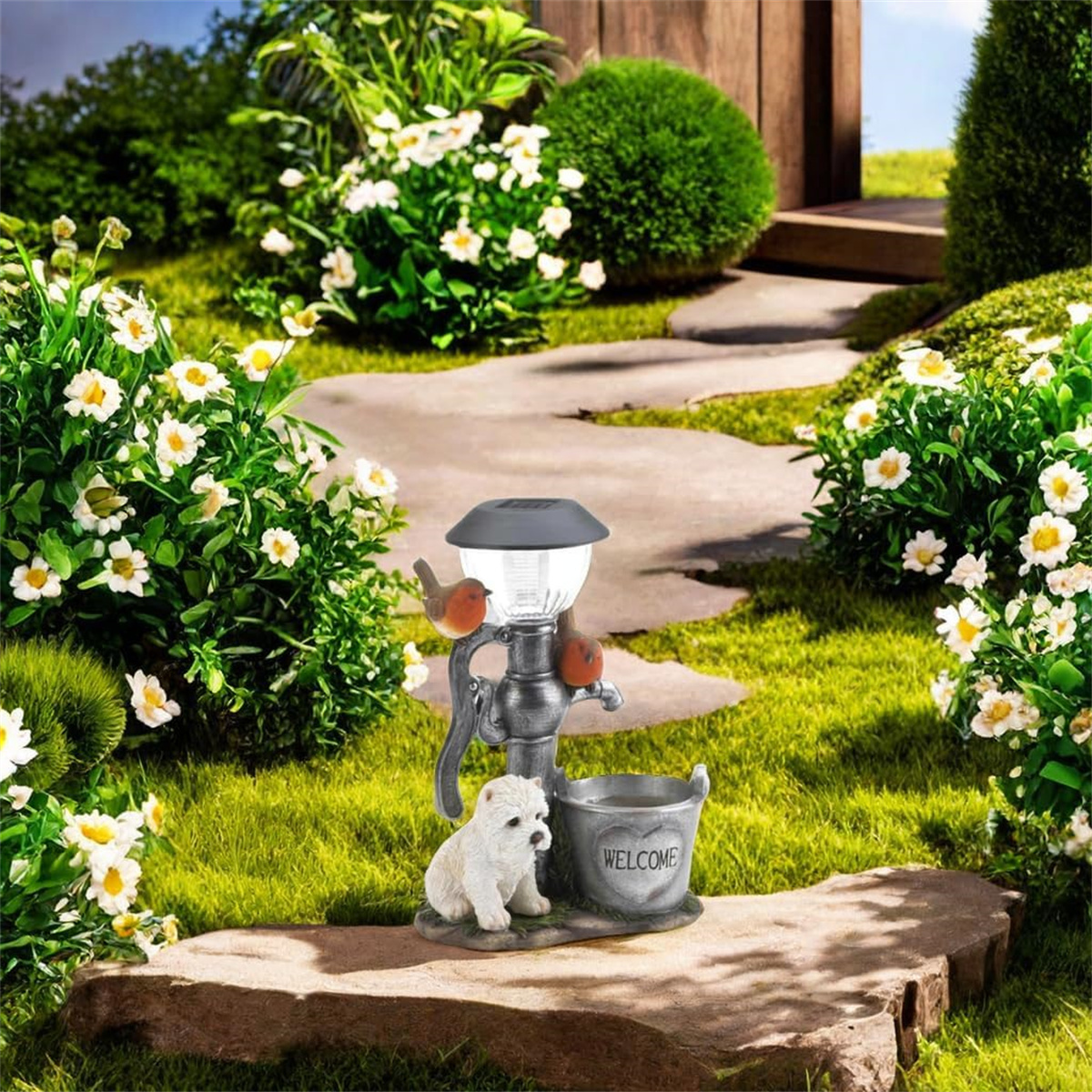 Solarbetriebener Springbrunnen mit Hundestatue und zwei Vogelstatuen. Grünes Gras und weiße Blumen drumherum.