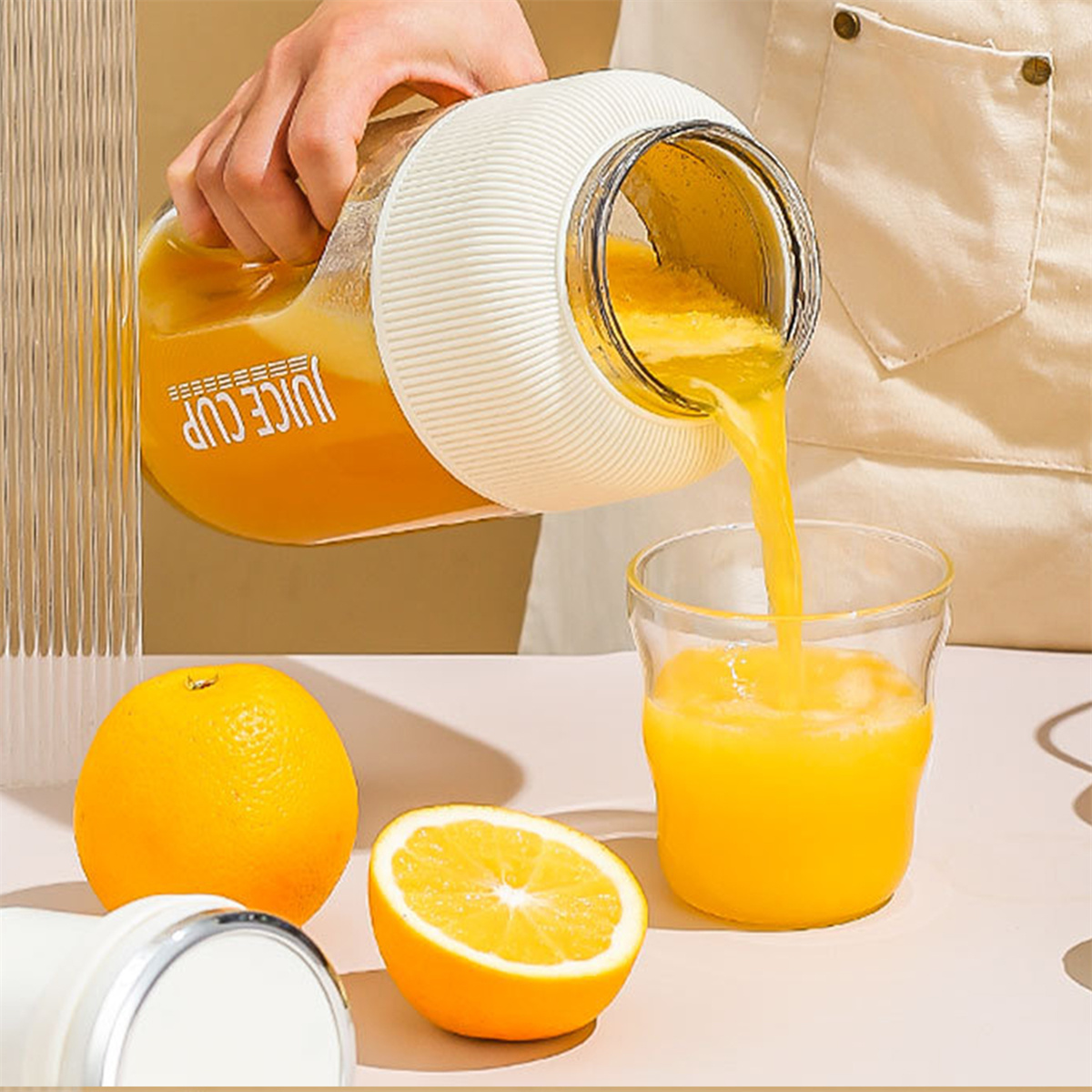 Hand gießt Orangensaft aus einem weißen und klaren Krug in ein Glas, mit Orangen.