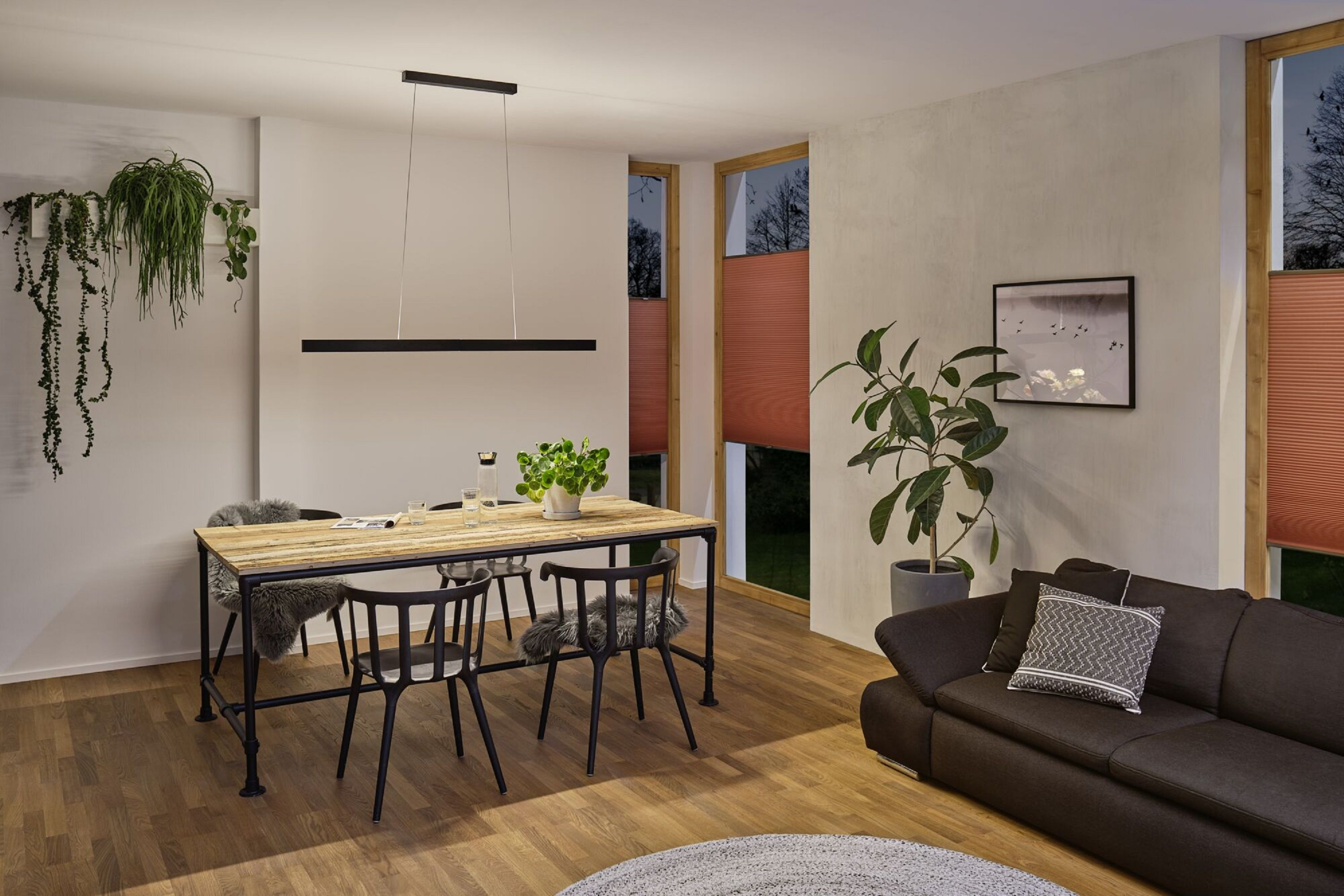 Jadalnia ze stołem, krzesłami i sofą. Wisząca lampa, rośliny i dzieła sztuki na ścianie.