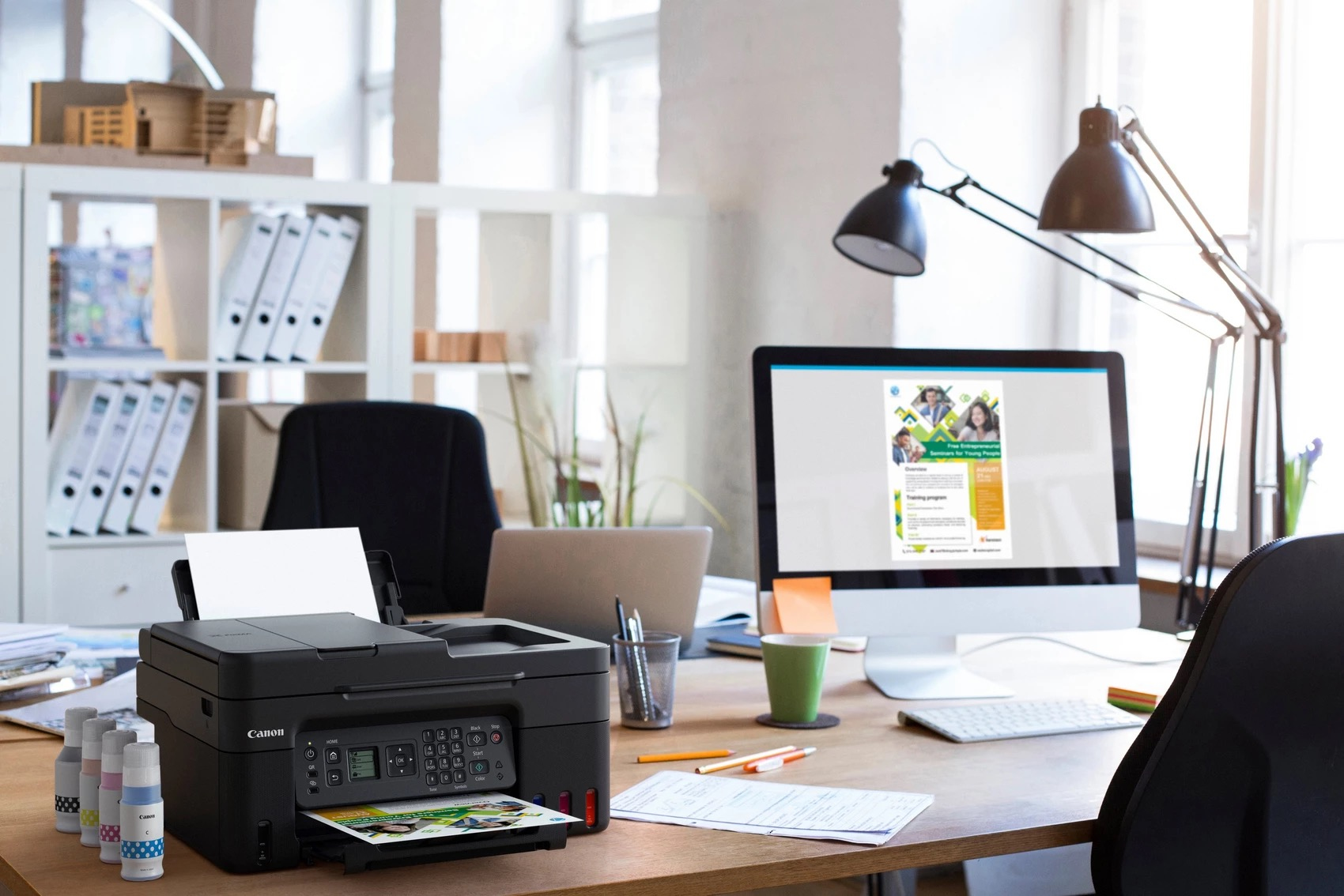 Drukarka na biurku z butelkami z tuszem i komputerem.