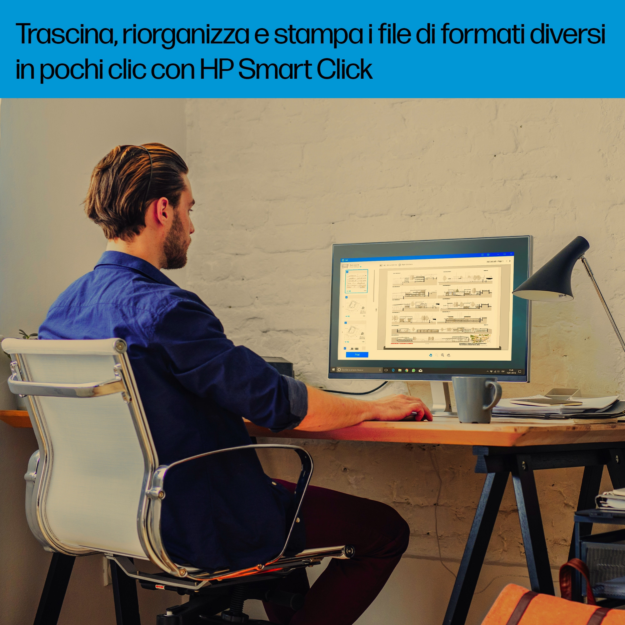 Uomo in camicia blu seduto a una scrivania, usa un computer. Una lampada e una tazza sono sulla scrivania.