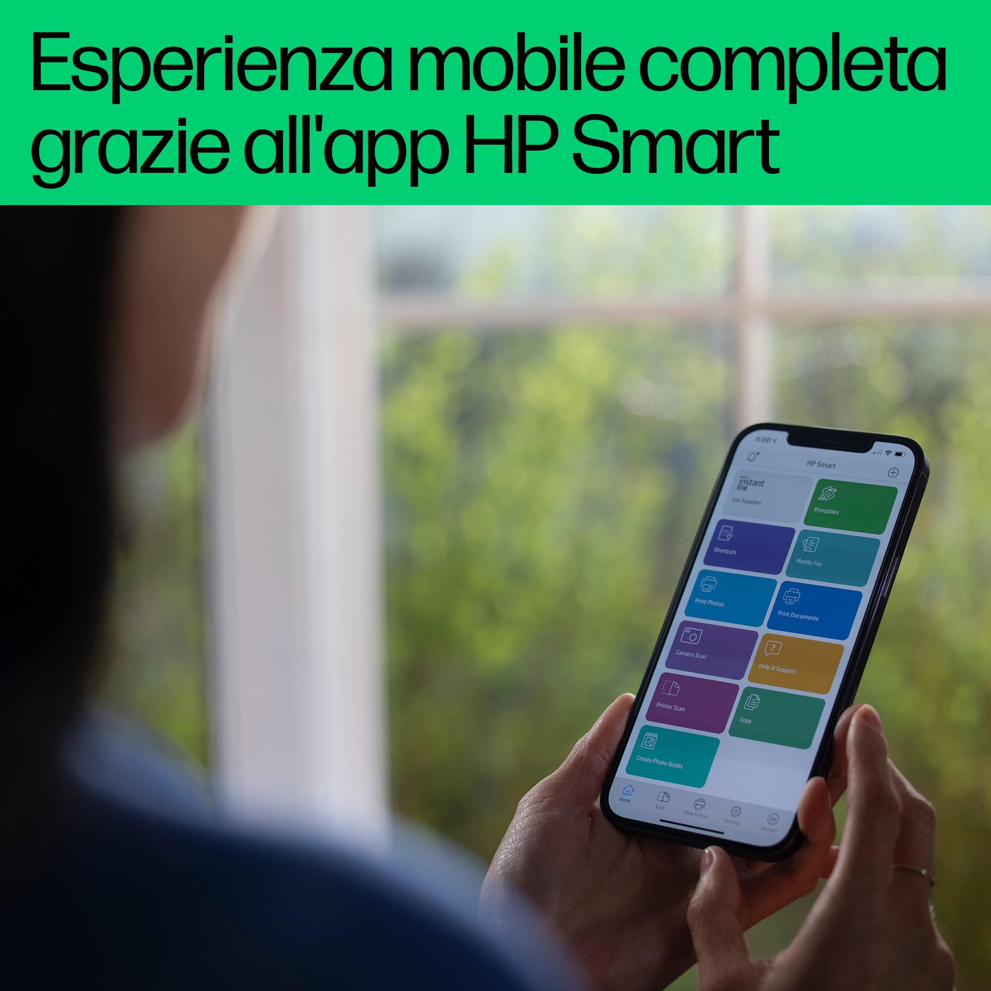 Dłonie osoby trzymającej telefon z otwartą aplikacją HP Smart. Tło to zielone okno.