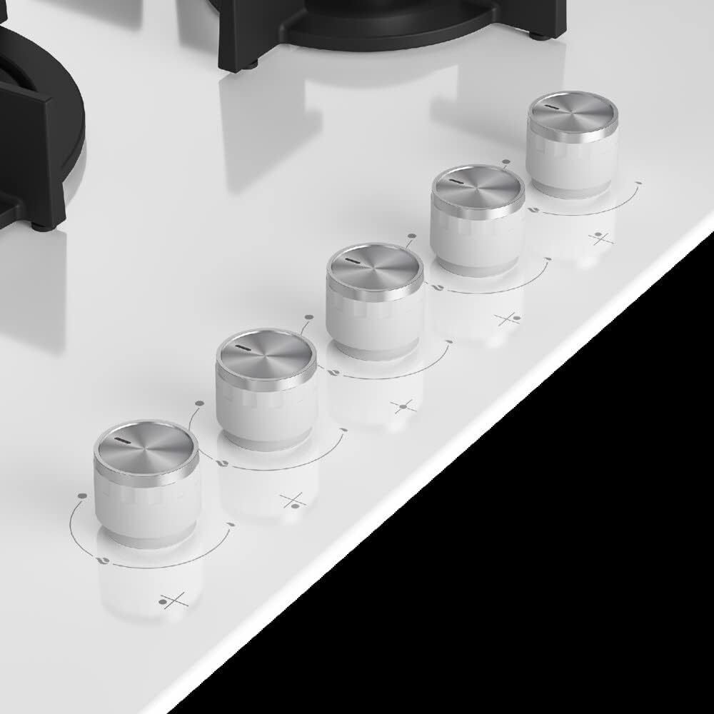 Zbliżenie pokręteł kuchenki gazowej. Białe pokrętła ze srebrnymi akcentami. Powierzchnia jest biała z czarnym blatem.