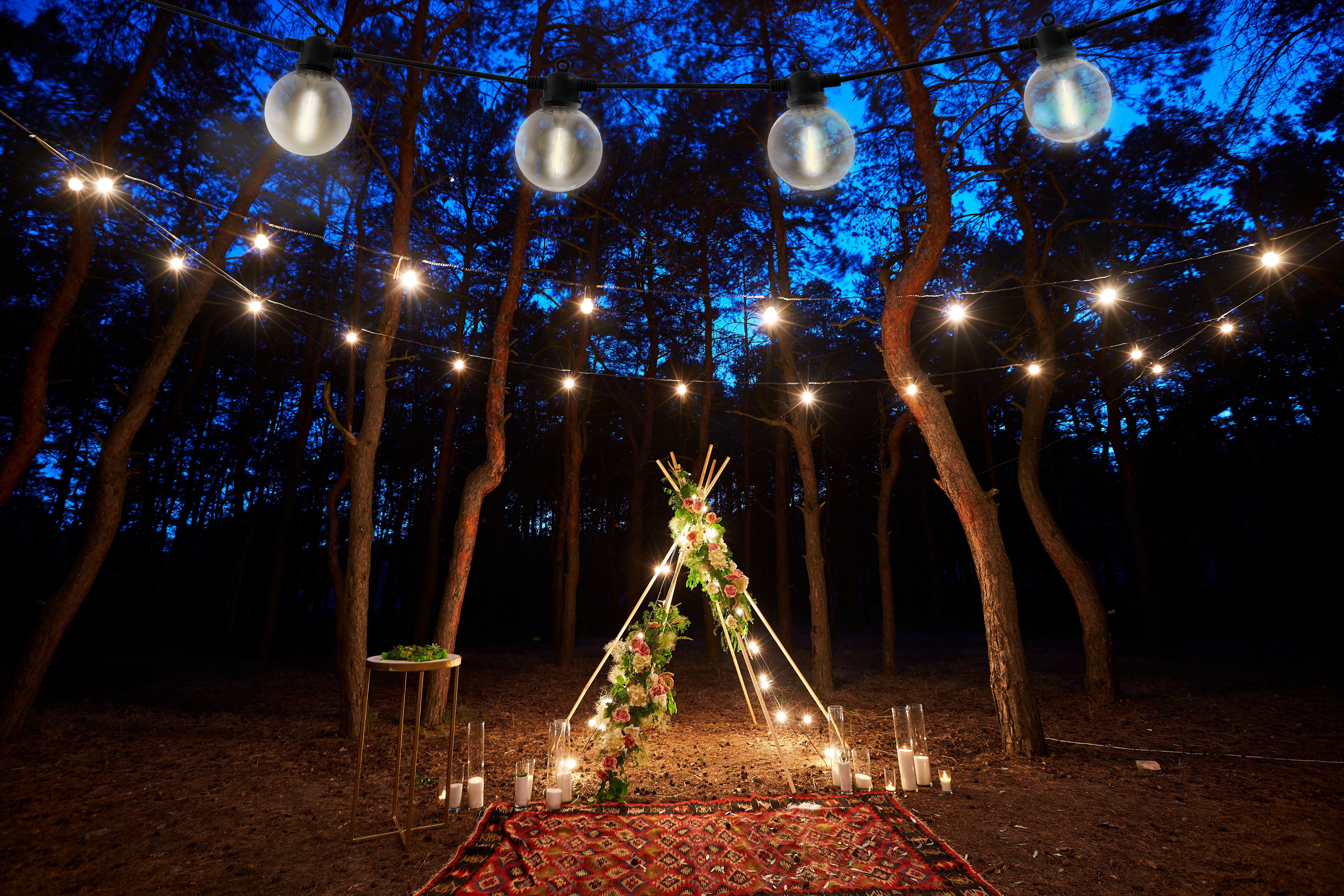 Nachtszenen mit Lichterketten, einem Blumenzelt, Kerzen und einem Waldhintergrund.